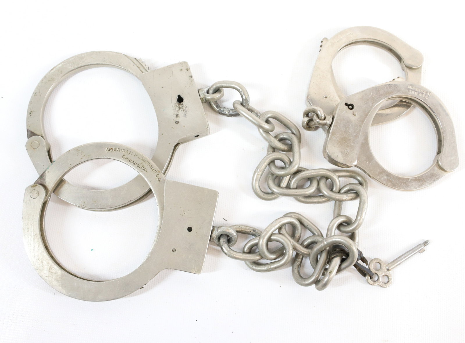 (2) PAIRS OF HANDCUFFS: AMERICAN MUNITIONS CO. CHICAGO, IL. AND POLICE HANDCUFF #186.674. MADE IN SPAIN. ONE SET WITH KEY. Registration: Terms: