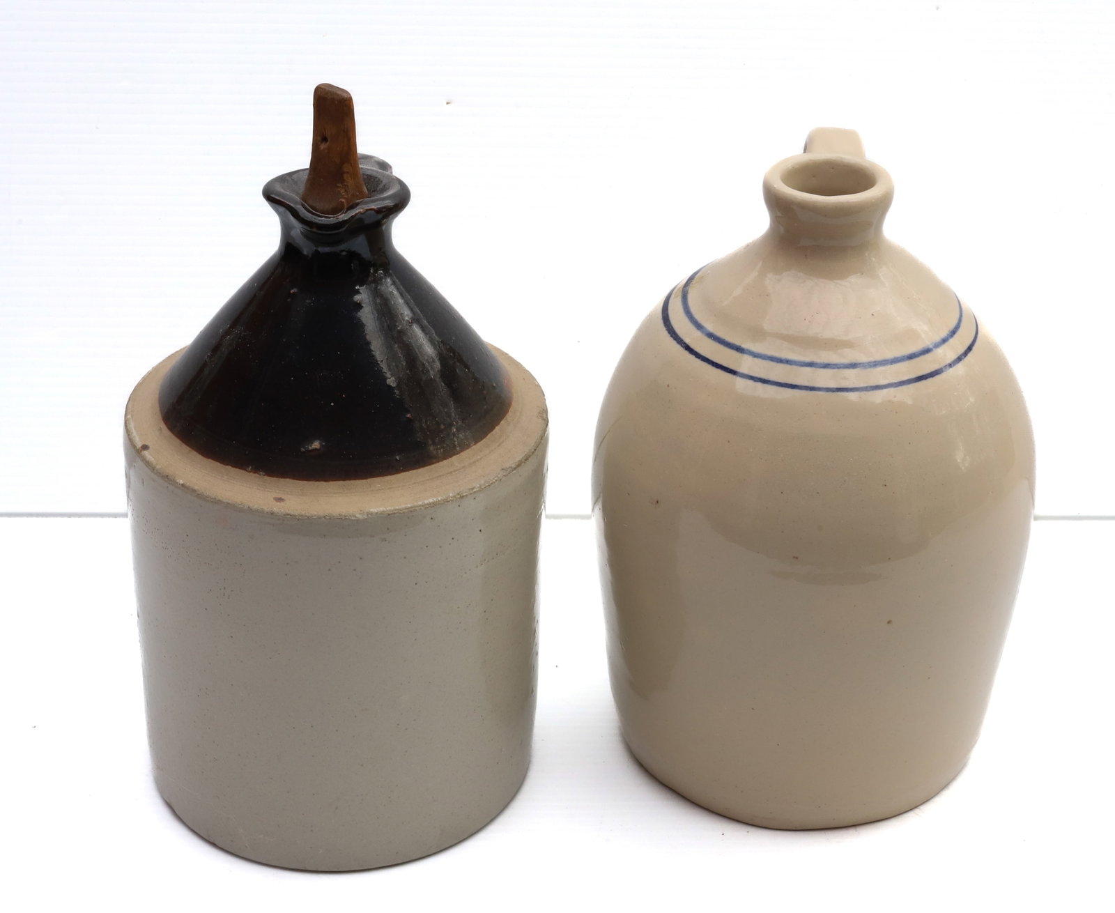 (2) STONEWARE JUGS: ONE WHITE WITH BLUE BANDING (STAMPED ON BOTTOM) BROWN AND WHITE GLAZE WITH WOODEN STOPPER - 11 1/4" H Terms: PLEASE READ CAREFULLY -THIS IS AN ONLINE ONLY AUCTION. Terms for Purchasing and Shipping of