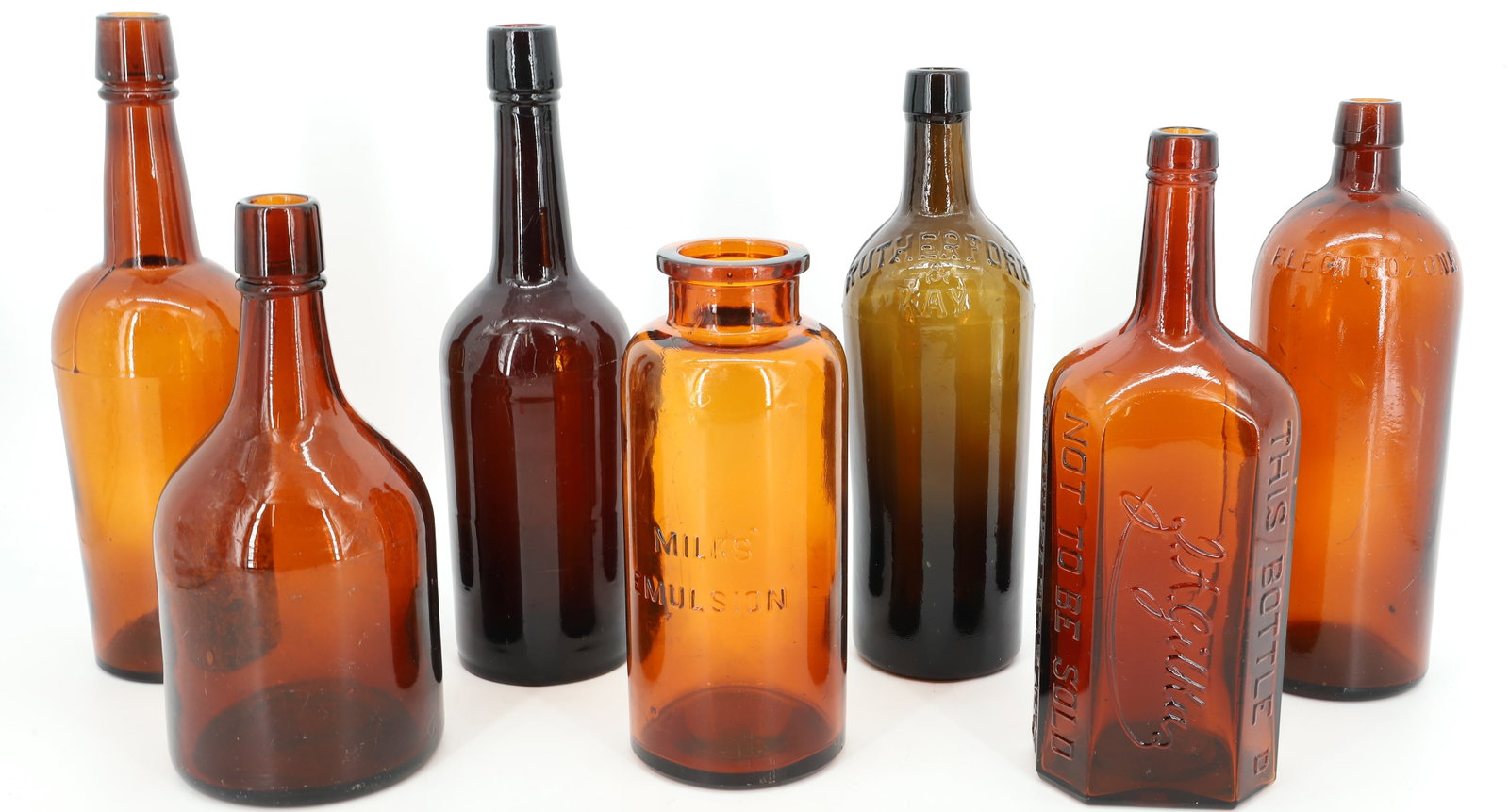LOT OF ANTIQUE AMBER BOTTLES: (7) INCLUDING: J.A. GILKA (BERLIN), "ELECTROZONE", "MILKS' EMULSION, "RUTHERFORD & KAY" AND MORE. 8 1/4" TO 11 1/4" HEIGHTS. PLEASE READ CAREFULLY - Terms for Purchasing and Shipping of Auction Items.