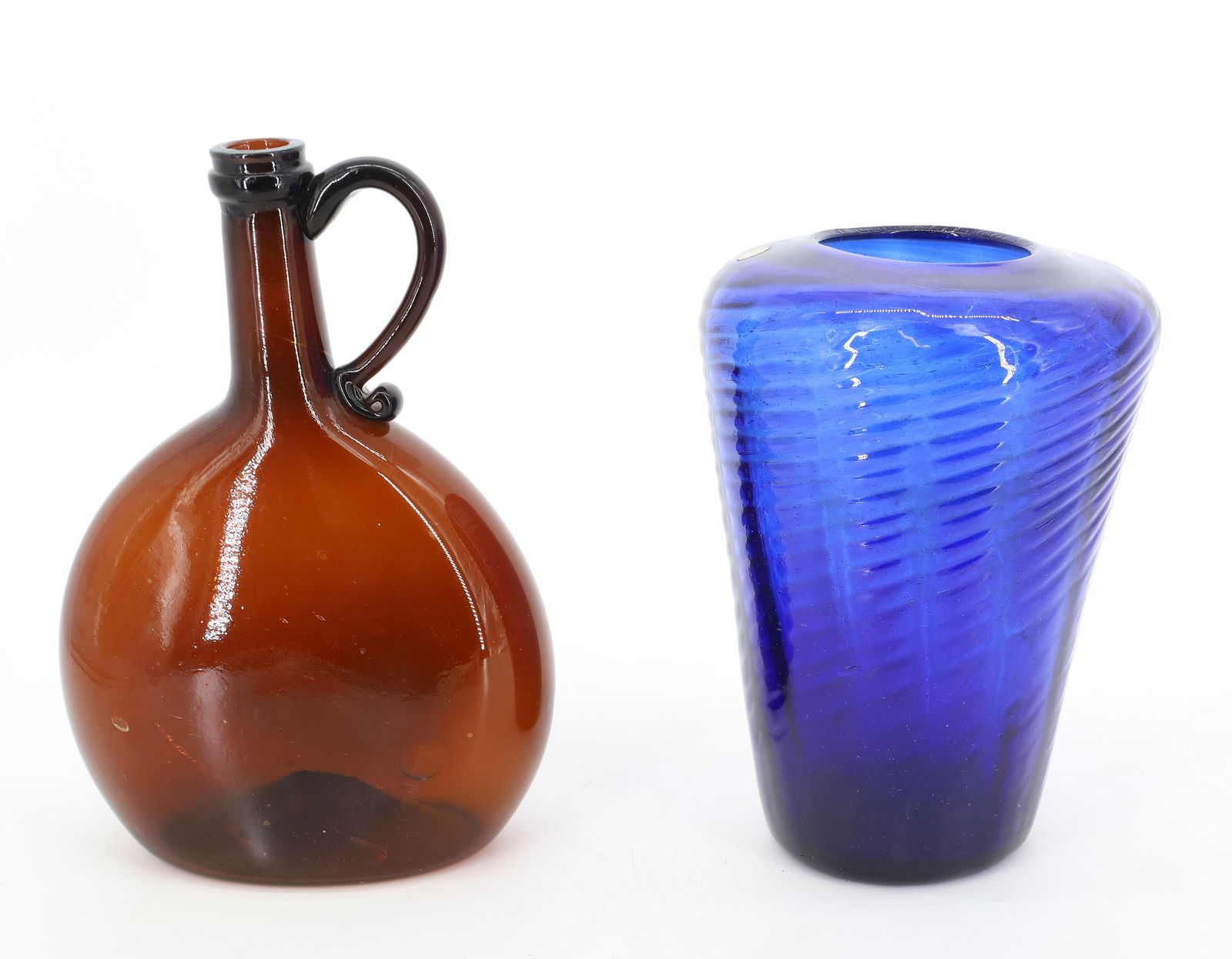 AMBER BLOWN GLASS HANDLED FLASK AND COBALT BLOWN GLASS VASE: AMBER FLASK WITH APPLIED HANDLE. ROUGH PONTIL. SOME BUBBLES. 9" X 6 1/4". SWIRL DESIGN VASE. ROUGH PONTIL. OLD LABEL ON TOP. 8" H. PLEASE READ CAREFULLY - Terms for Purchasing and Shipping of Auction