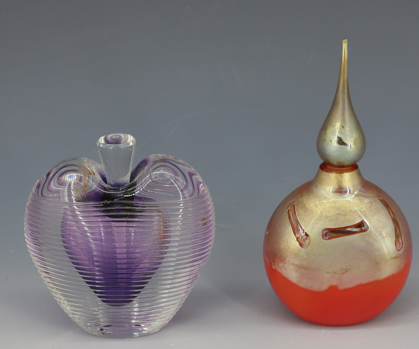 (2) ART GLASS PERFUME BOTTLES: AMETHYST COLOR HEART SHAPE WITH APPLIED THREADING ZELLIQUE STUDIO AND ROLAND ORANGE AND GOLD IRIDESCENT STEEPLE STOPPER 3 1/2"H,5"H PLEASE READ CAREFULLY - Terms for Purchasing and Shipping of Auction