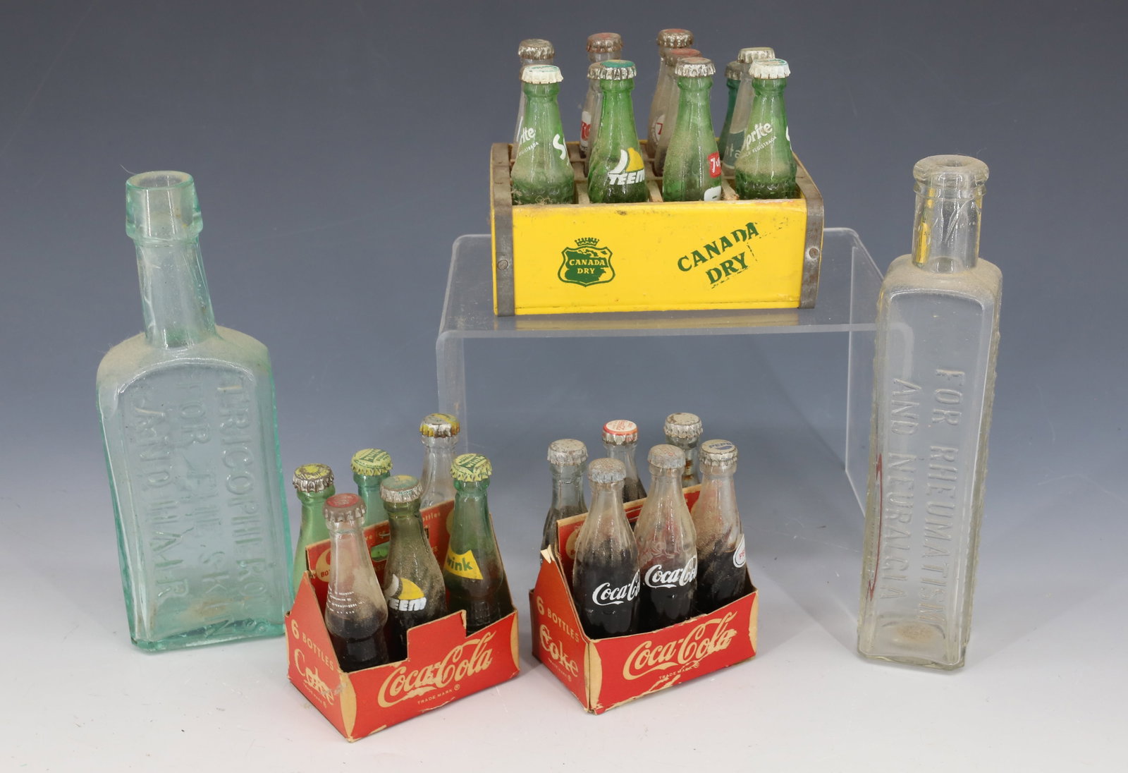 LOT OF MINIATURE BOTTLES: MINI SODA POP BOTTLES IN COKE AND CANADA DRY CARRIERS. BOTTLES AVERAGE 2 3/4" H. PLUS, TWO MEDICAL BOTTLES (CLARK STANLEY'S SNAKE OIL LINIMENT AND BARRY'S TRICOPHEROUS FOR THE SKIN AND HAIR. 6" H. PLE