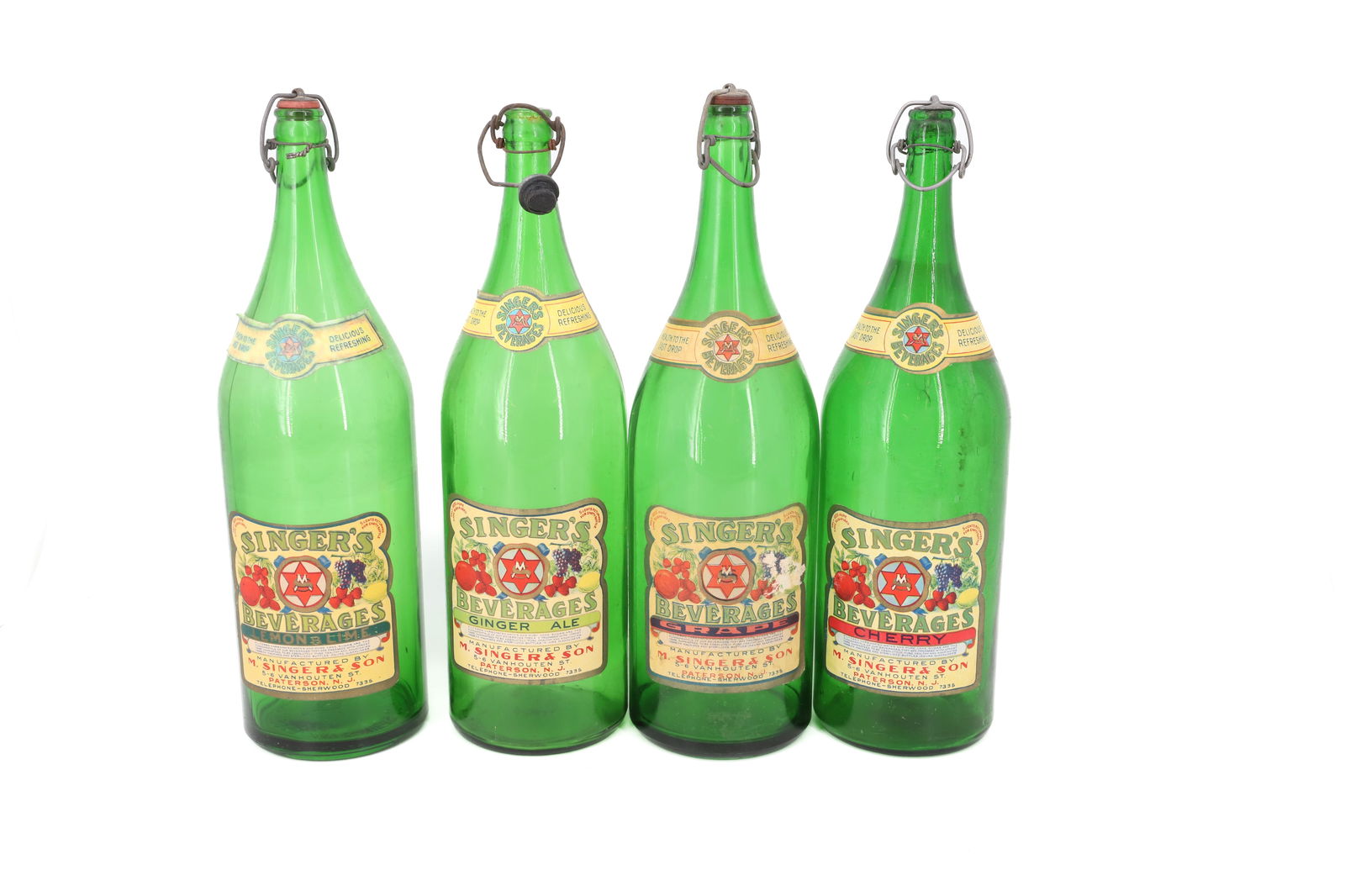 (4) SINGER'S BEVERAGE BOTTLES: GREEN WITH PAPER LABELS (GINGER ALE, GRAPE, CHERRY AND LEMON/LIME). 14 1/4" H. PLEASE READ CAREFULLY - Terms for Purchasing and Shipping of Auction Items. Please read carefully before bidding. Hartzel