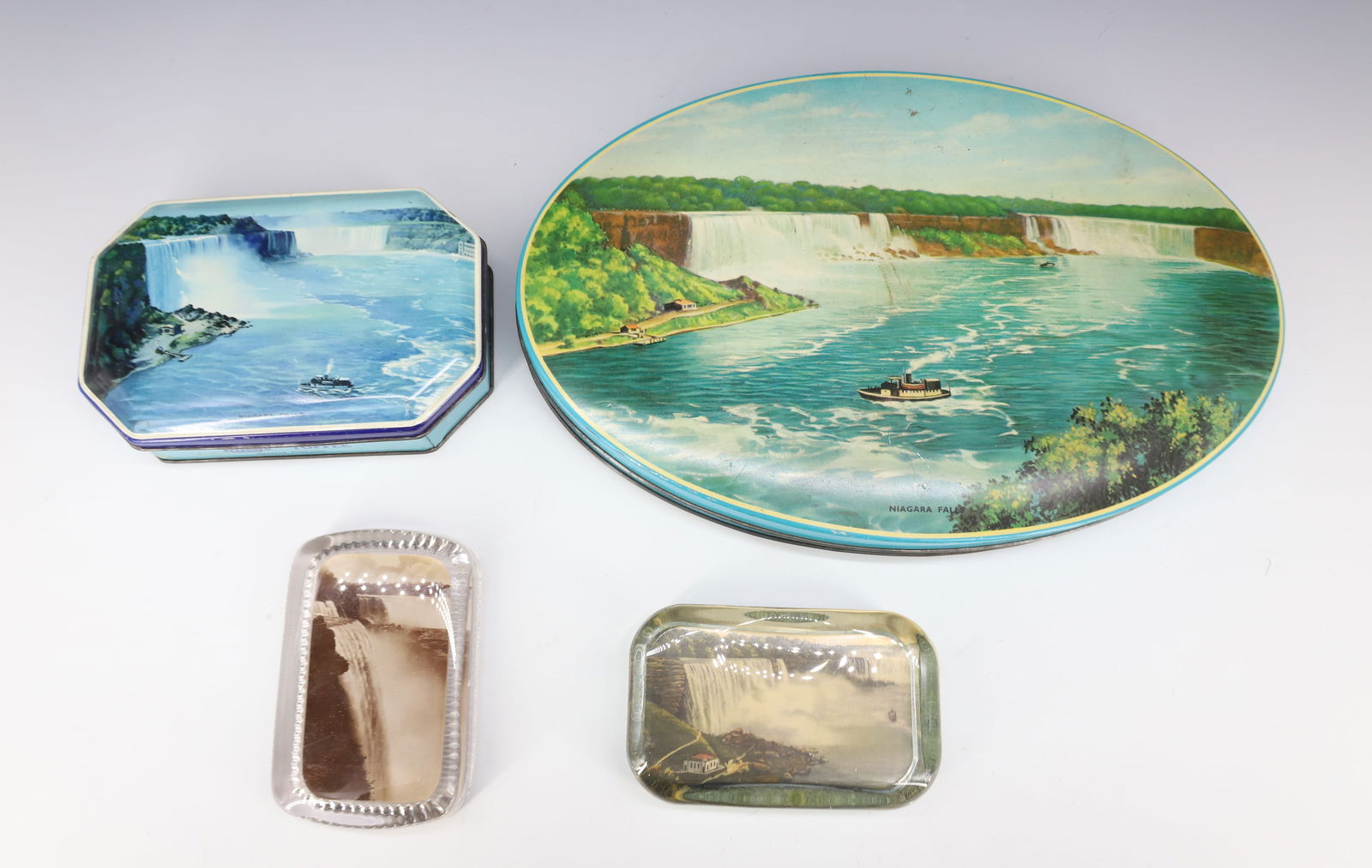 NIAGARA FALLS PAPERWEIGHTS AND TINS: TWO GLASS PAPERWEIGHTS AND TWO TINS. LARGEST 11" L. PLEASE READ CAREFULLY - Terms for Purchasing and Shipping of Auction Items. Please read carefully before bidding. Hartzell’s Auction Gallery.