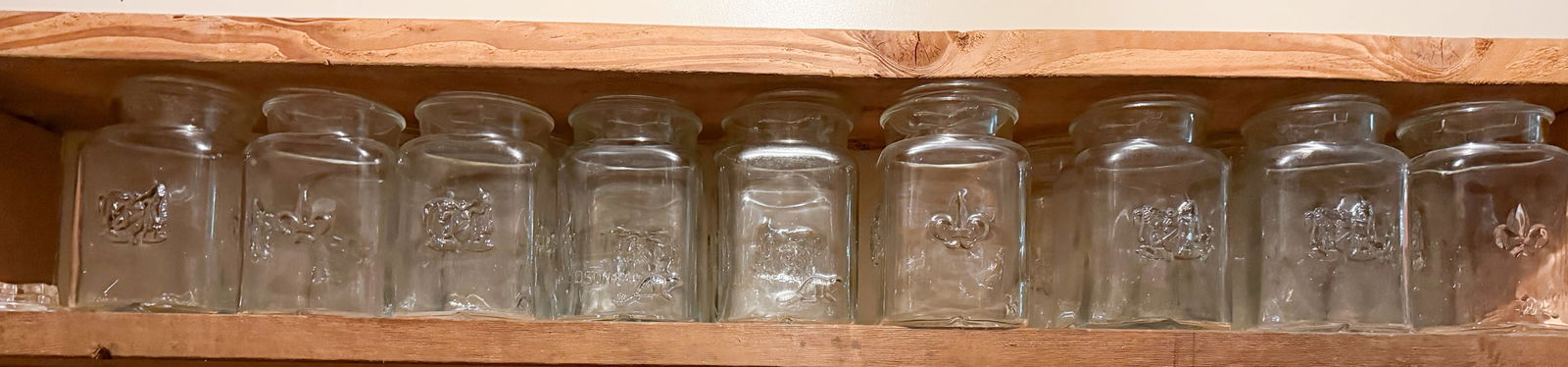 (16) HUDSON BAY GLASS STORAGE JARS: EMBOSSED NAMES AND DESIGNS WITH LIDS - 8 1/2" H CONDITION REPORTS ARE BASED ON VISUAL INSPECTION. IF YOU HAVE ANY FURTHER QUESTIONS REGARDING CONDITION OF AN ITEM, PLEASE CONTACT US FOR A MORE DETAILE