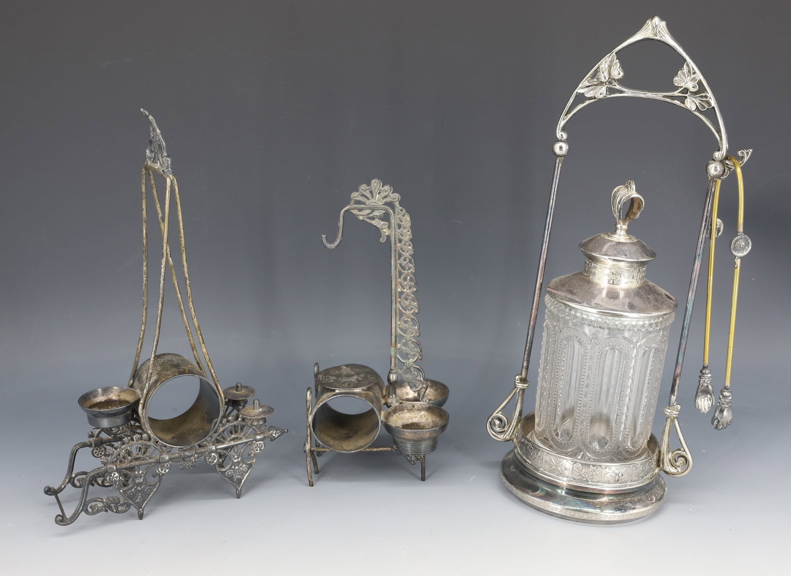 VICTORIAN PICKLE CASTER AND HOLDERS: PRESSED GLASS JAR AND SILVERPLATE HOLDER / TONGS 12 3/8" H. WITH, TWO ORNATE EASTLAKE HOLDERS. LARGEST 10" H. PLEASE READ CAREFULLY - Terms for Purchasing and Shipping of Auction Items. Please read ca