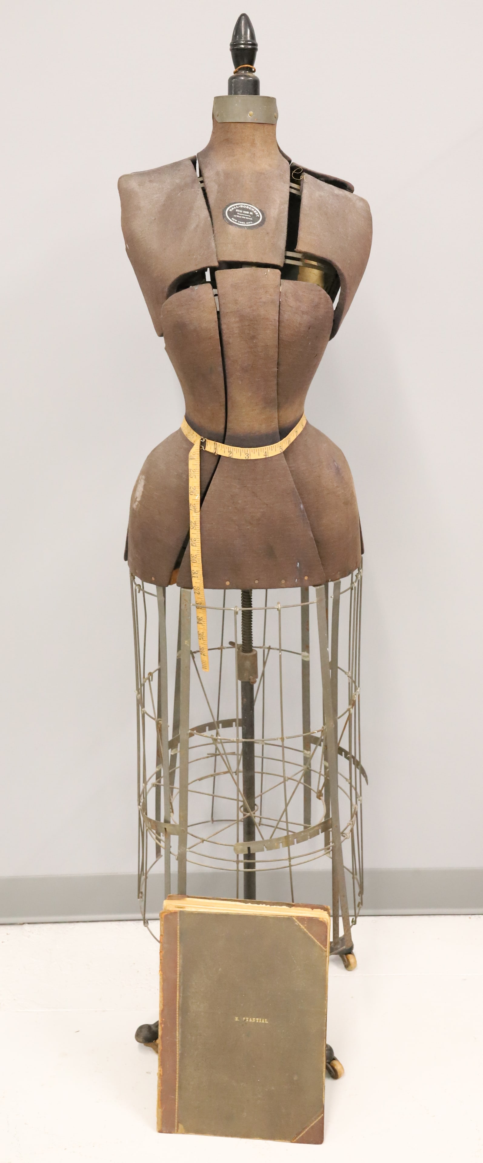 ANTIQUE DRESS FORM AND PATTERN BOOK: HALL-BORCHERT DRESS FORM WITH "FRANK LESLIE'S GAZETTE OF FASHION AND THE BEAU MONDE, 1857" BELONGING TO MARIAH STANHEL DUNSTER. BOOK CONTAINS SEVERAL COLOR PRINTS AND PAPER PATTERNS. FORM 63" H. ADJUS