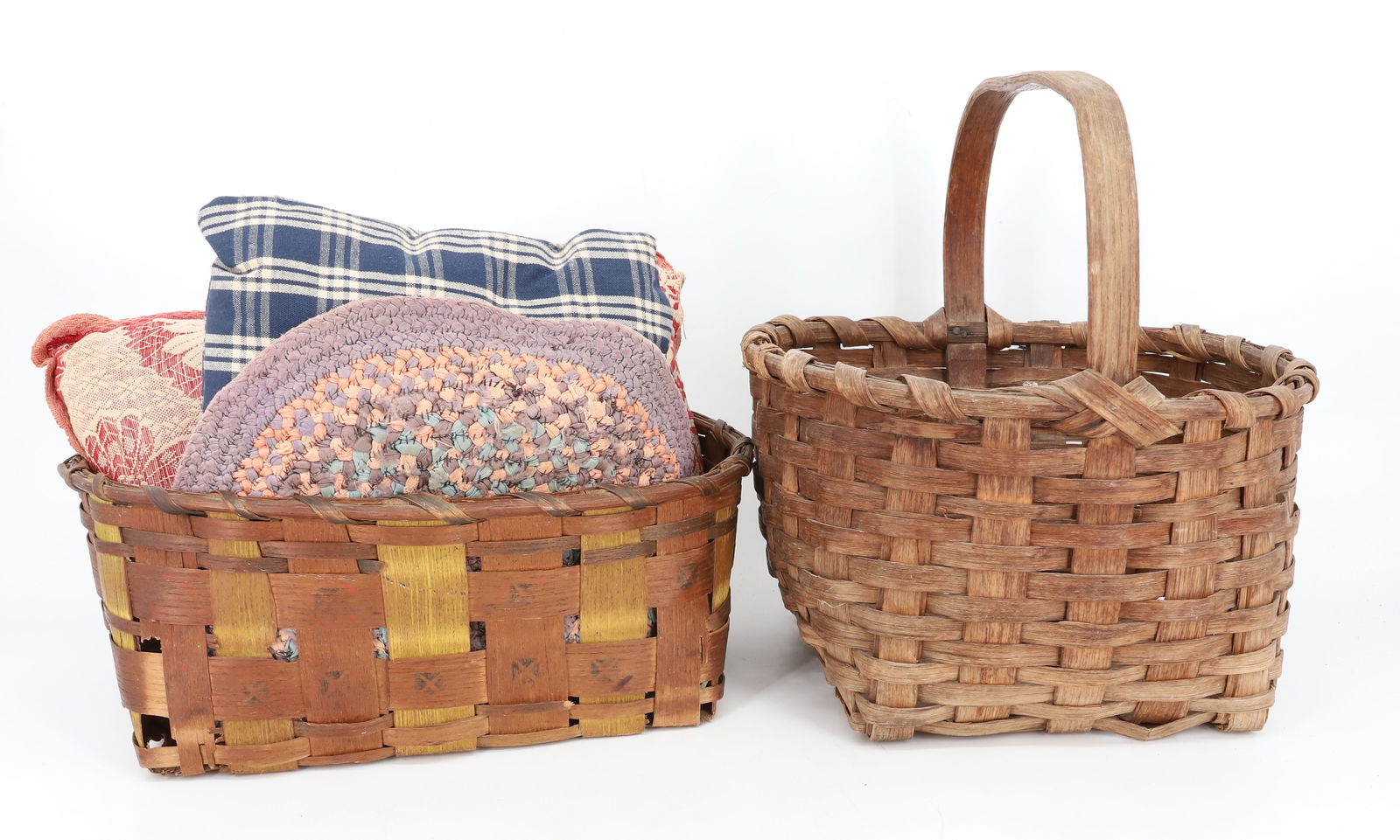 ANTIQUE BASKETS AND TEXTILES: TWO WOVEN BASKETS. HANDLELESS BASKET HAS POTATO STAMP DECORATION 13" L, TWO SMALL PILLOWS AND BRAIDED TABLE MAT. 11 1/2" D. PLEASE READ CAREFULLY - Terms for Purchasing and Shipping of Auction Items.