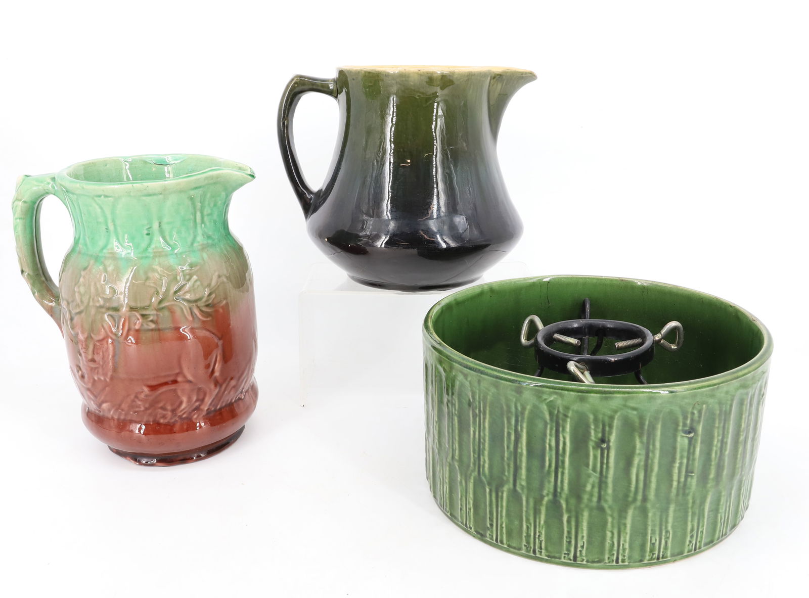 POTTERY TREE STAND AND PITCHERS: GREEN GLAZED POTTERY TREE STAND WITH METAL INSERT 4 3/4" X 9". WITH TWO GLAZED PITCHERS. TALLER HAS EMBOSSED DECORATION WITH MULTI-COLOR GLAZE 8 1/2" H. YELLOW WARE BODY PITCHER WITH STREAKY GREEN GLA