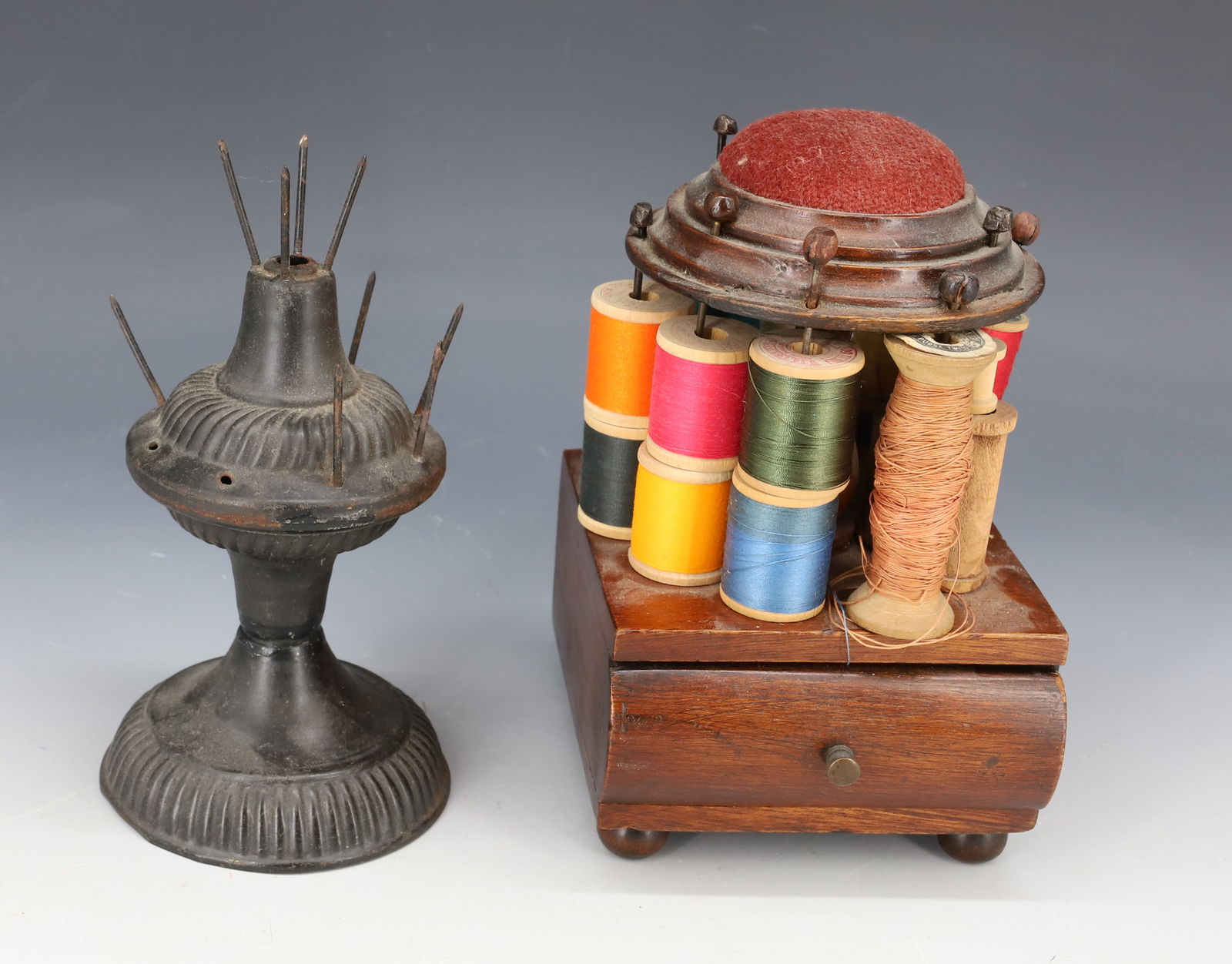(2) SEWING SPOOL HOLDERS / PIN CUSHION: PRESSED METAL SPOOL HOLDER MRKD. CPF 6 1/2" H. WITH, WOODEN HOLDER WITH SINGLE DRAWER AND PIN CUSHION TOP 7" H. PLEASE READ CAREFULLY - Terms for Purchasing and Shipping of Auction Items. Please read