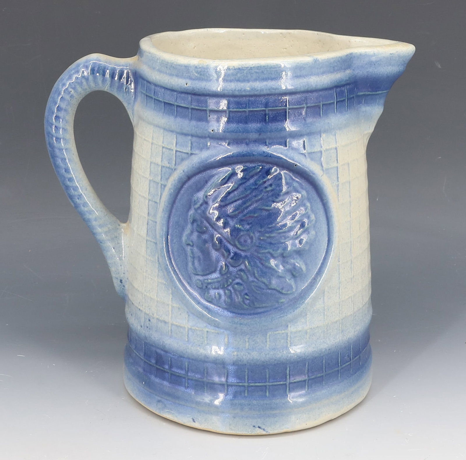 SALT-GLAZED EMBOSSED INDIAN PITCHER: BLUE/WHITE WITH INDIAN CHIEF ON EITHER SIDE. 8" H. PLEASE READ CAREFULLY - Terms for Purchasing and Shipping of Auction Items. Please read carefully before bidding. Hartzell’s Auction Gallery. H