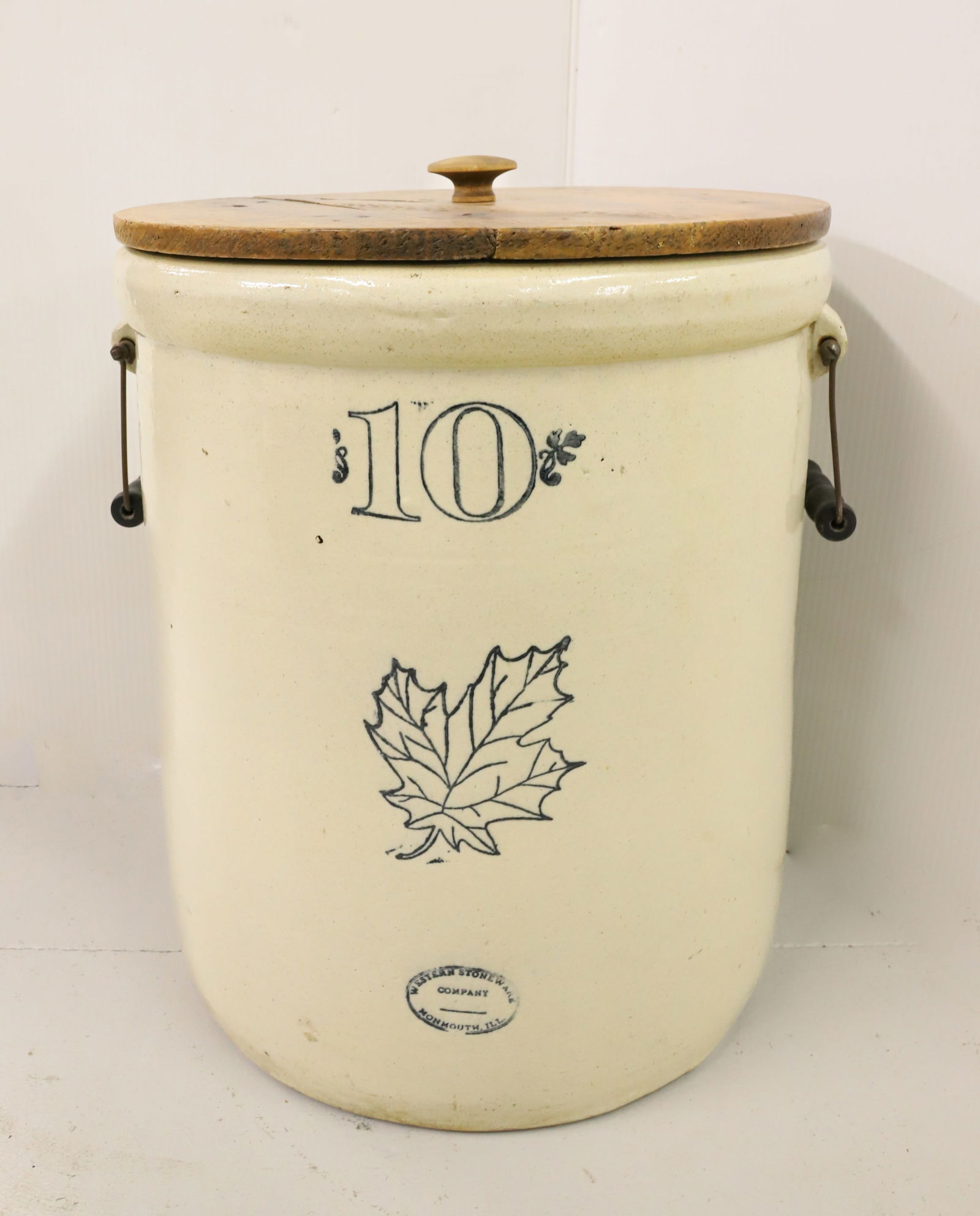10-GALLON WESTERN STONEWARE CROCK: STAMPED "10" AND LEAF ON FRONT ABOVE "WESTERN STONEWARE COMPANY, MONMOUTH, ILL" WIRE HANDLES ON EITHER SIDE. WITH WOODEN COVER. 17 1/2" X 15 1/2". HEAVY WEIGHT. PLEASE READ CAREFULLY - Terms for Purch
