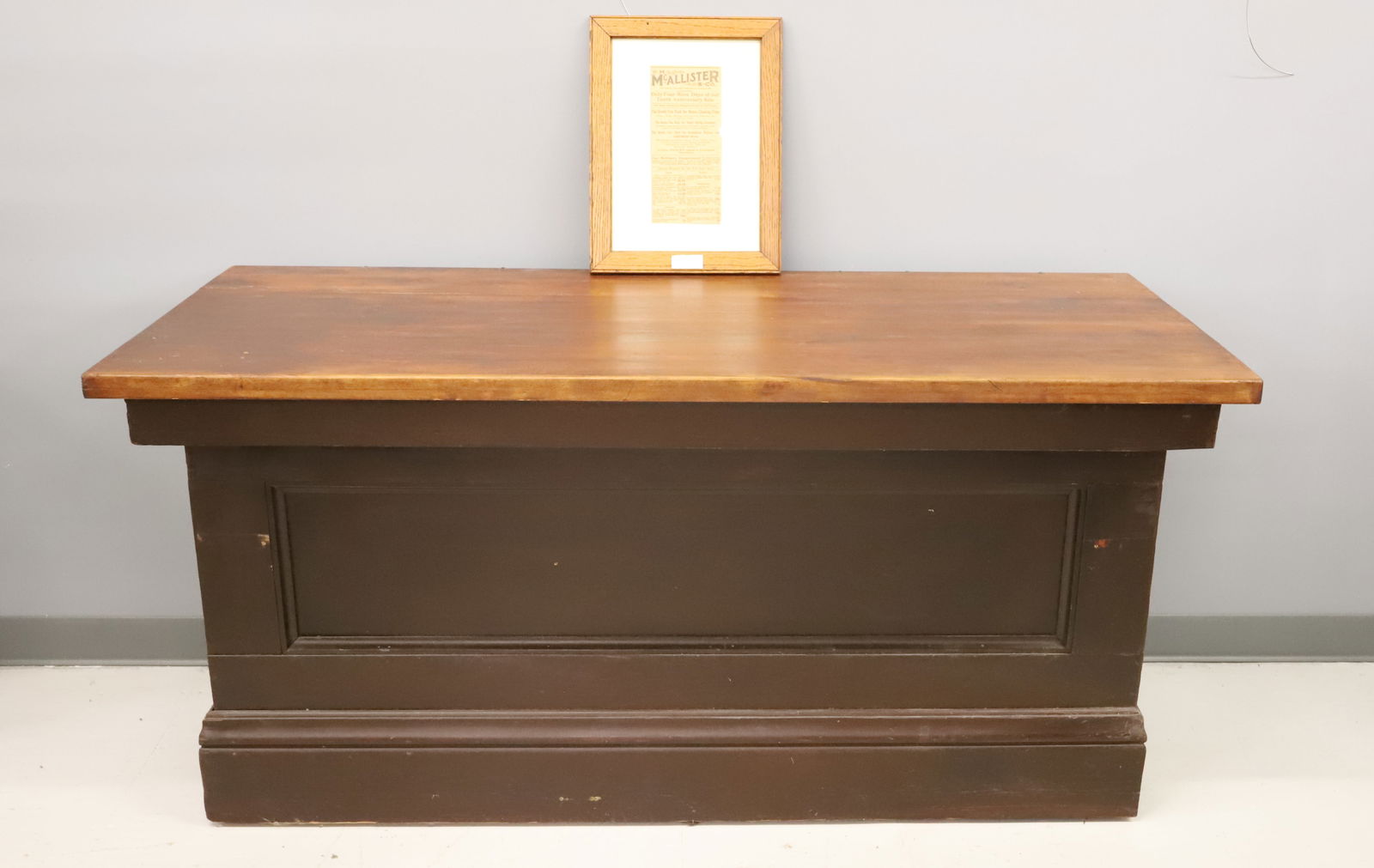 WOODEN COUNTRY STORE COUNTER: PANELED FRONT AND ENDS PAINTED BROWN. UNPAINTED TOP AND OPEN BACK. FROM "WM. MCALLISTER STORE" FRAMED ADVERTISEMENT. 30" X 60" X 26". PLEASE READ CAREFULLY - Terms for Purchasing and Shipping of Aucti