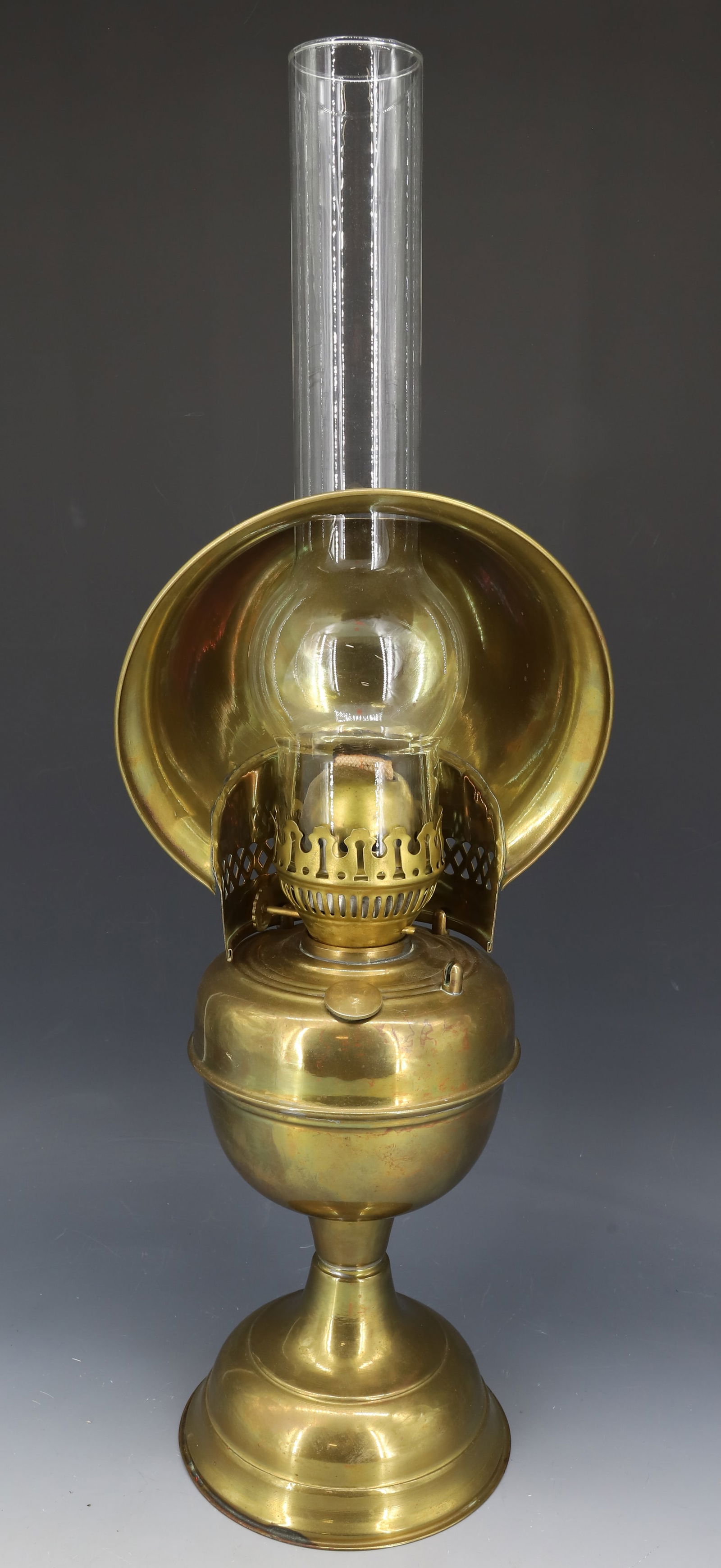 BRASS OIL LAMP: PEDESTAL LAMP WITH GLASS CHIMNEY AND BRASS REFLECTOR. TOTAL SIZE 23". PLEASE READ CAREFULLY - Terms for Purchasing and Shipping of Auction Items. Please read carefully before bidding. Hartzell’s