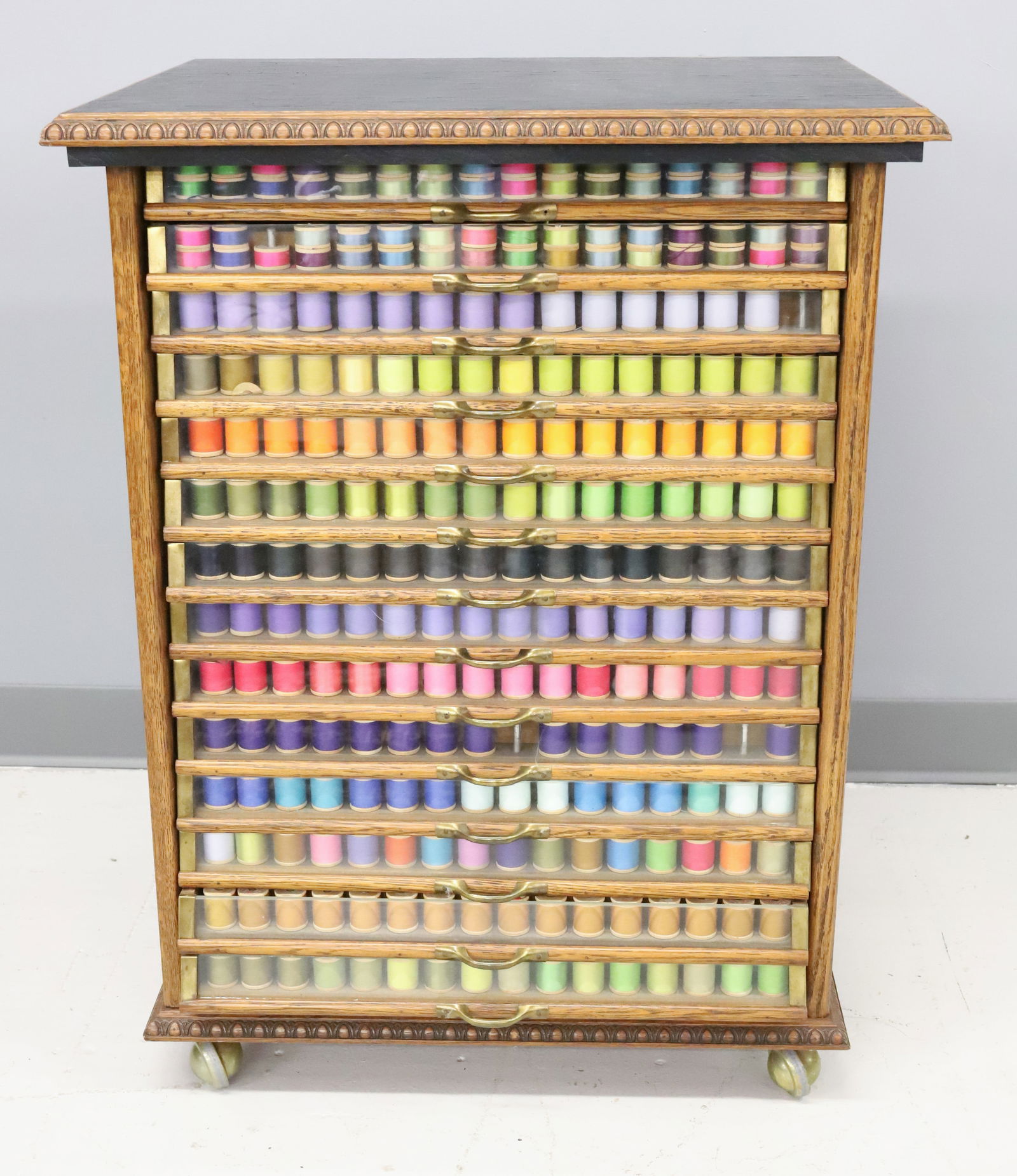 LARGE OAK SPOOL CABINET: 14-DRAWERS WITH GLASS FRONTS. OAK CASE WITH PANELED SIDES. CONTEMPORARY WHEELS ADDED. 31 1/4" X 24" X 19". PLEASE READ CAREFULLY - Terms for Purchasing and Shipping of Auction Items. Please read caref