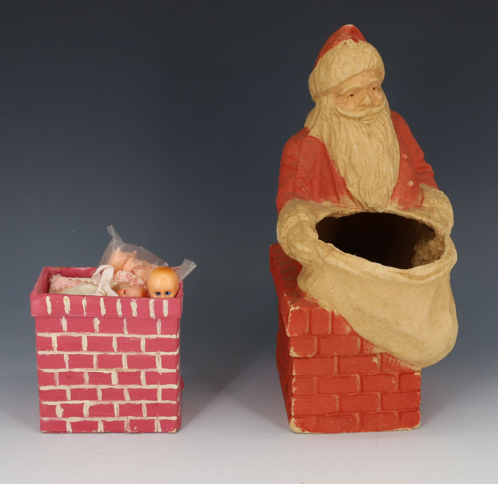 SANTA CLAUS CANDY CONTAINER: PRESSED CARDBOARD SANTA WITH SACK / CHIMNEY. 9 1/2" H. PLUS, SMALL CHIMNEY FILLED WITH MOLDED PLASTIC DOLL PARTS.