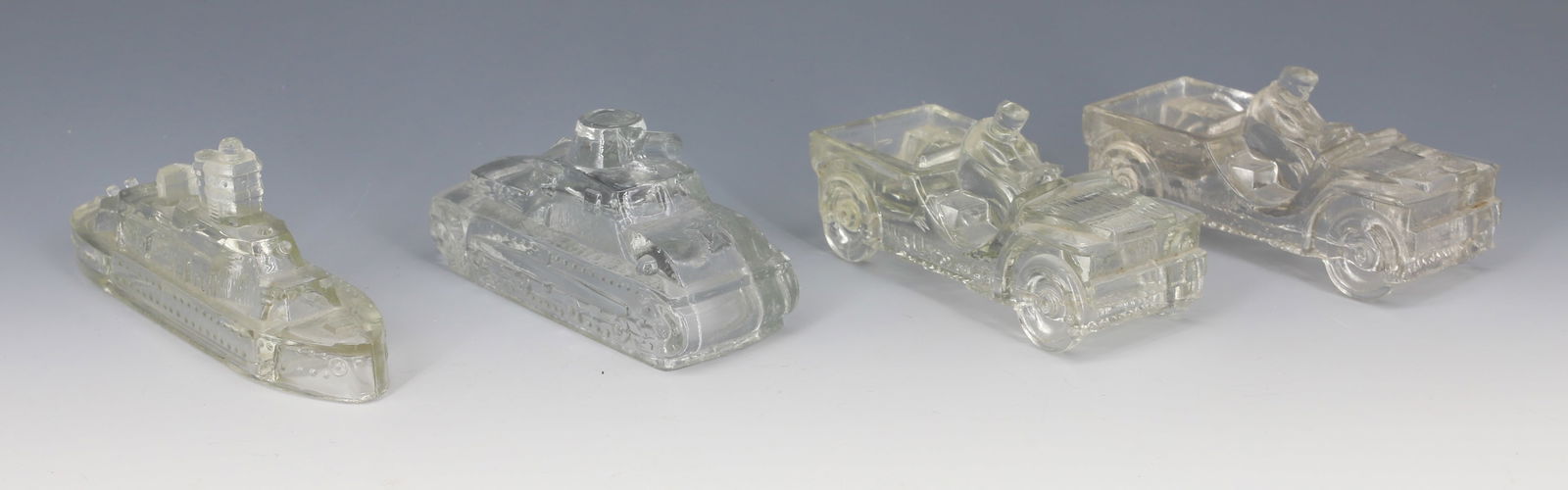(4) GLASS MILITARY CANDY CONTAINERS: INCLUDING: BATTLESHIP 5 3/8", TWO JEEPS (EMBOSSED WILLY'S JEEP ON SIDES AND MRKD. "J.H. MILL STEIN CO., JEANETTE, PA" AND ARMY TANK.