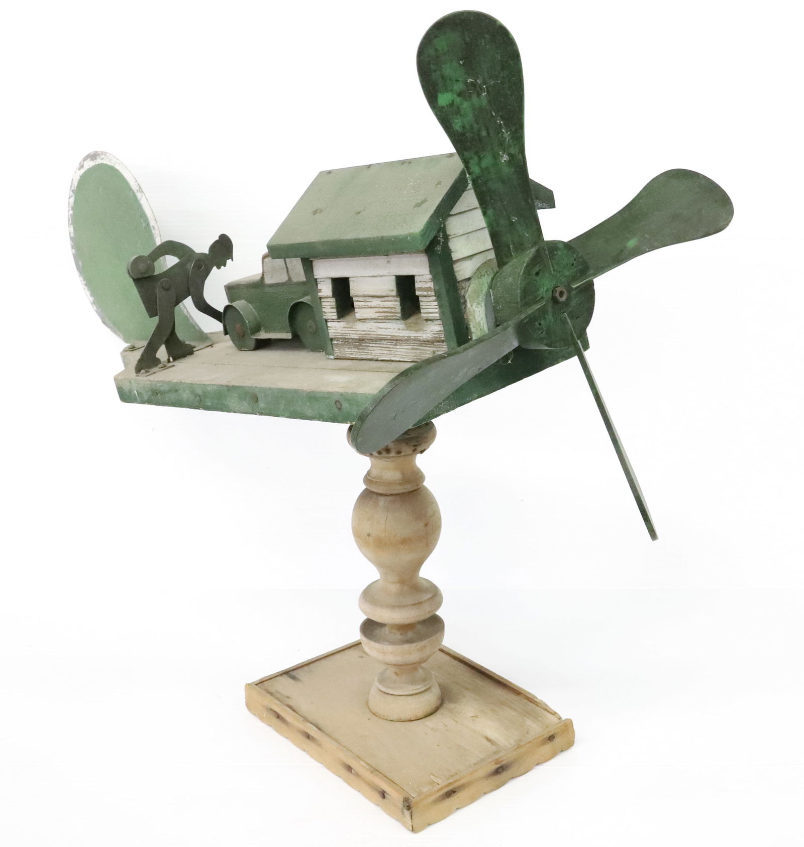 FOLK ART WOODEN WHIRLYGIG: GREEN / WHITE PAINTED WOOD AND METAL WITH MAN CRANKING CAR ENGINE. DISPLAYED ON WOODEN TURNED BASE. 26 1/2" X 32". PLEASE READ CAREFULLY - ITEMS MUST BE PAID FOR THROUGH LIVE AUCTIONEERS OR WITH