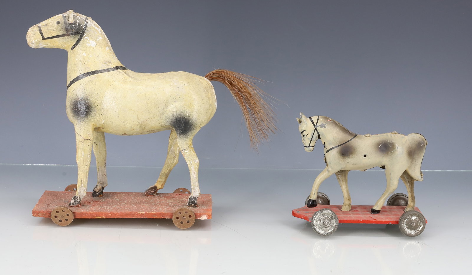 (2) TOY HORSES ON WHEELS: LARGER IS DECORATED COMPOSITION ON WOODEN PLATFORM. 7" X 6". SMALLER IS TIN LITHO. 4" X 4 1/4". PLEASE READ CAREFULLY - ITEMS MUST BE PAID FOR THROUGH LIVE AUCTIONEERS OR WITH CASH OR CHECK IN PERSON
