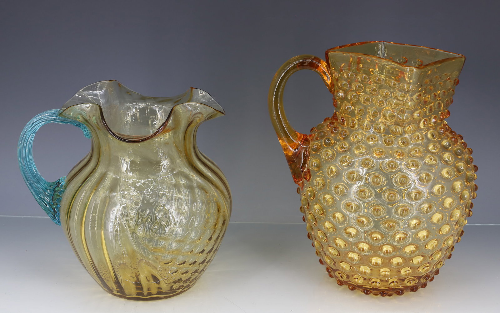 (2) VICTORIAN ART GLASS PITCHERS: PATTERN MOLDED AMBER BODY WITH BLUE REEDED APPLIED HANDLE, AMBER HOBNAIL SQUARE TOP APPLIED HANDLE POLISHED PONTILS 7 1/2"H, 9"H PLEASE READ CAREFULLY - ITEMS MUST BE PAID FOR THROUGH LIVE AUCTIONEERS