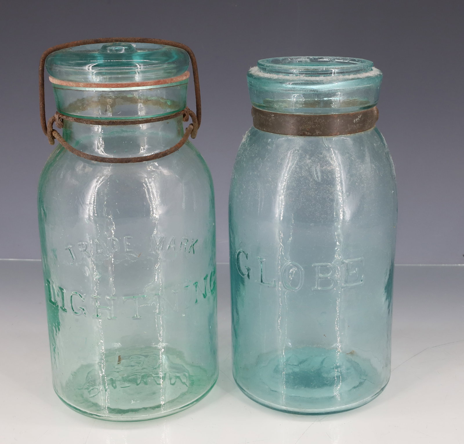GLOBE AND LIGHTNING FRUIT JARS: AQUA "GLOBE" JAR WITH TIN BAND AROUND NECK. MRKD. 66 ON BOTTOM. 7 1/2" H. "TRADEMARK LIGHTNING" JAR WITH LID AND WIRE CLOSURE. MRKD. PUTNAM 250 ON BOTTOM. 7 3/4" H. PLEASE READ CAREFULLY - ITEMS MUST