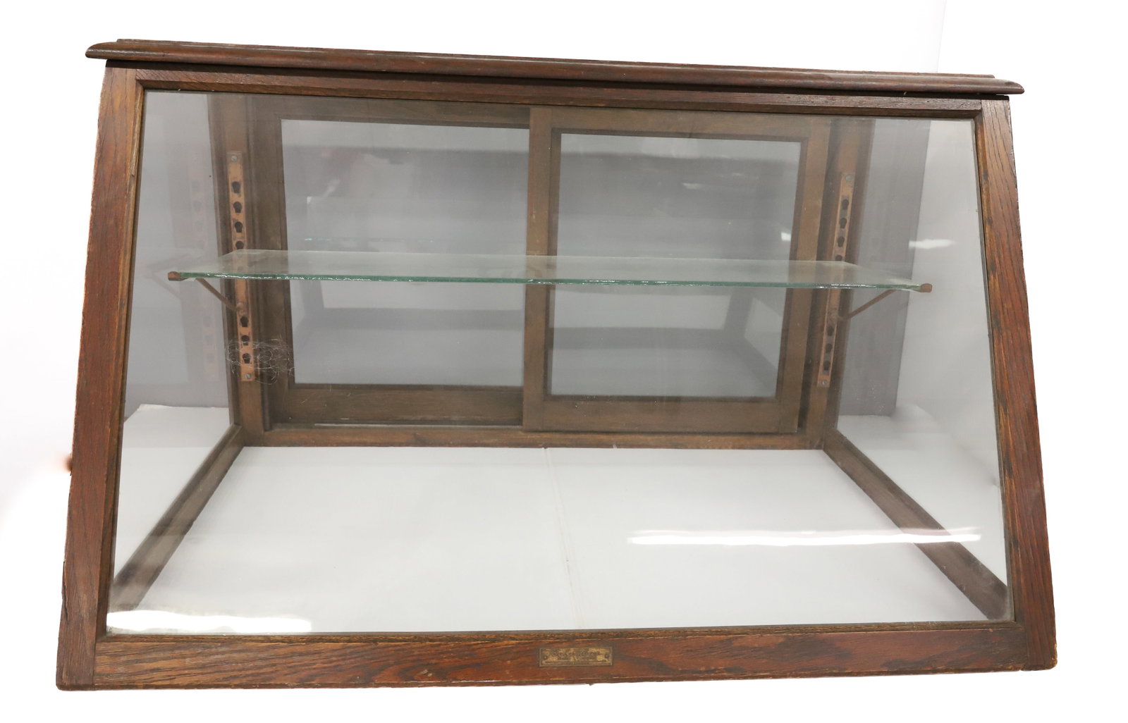 OAK SLANT FRONT SHOWCASE: COLUMBUS, GLASS SLIDING DOORS WITH GLASS SHELF, NO BOTTOM - 20 1/2" X 23 1/2" X 34 1/2" PLEASE READ CAREFULLY - ITEMS MUST BE PAID FOR THROUGH LIVE AUCTIONEERS OR WITH CASH OR CHECK IN PERSON - Terms 