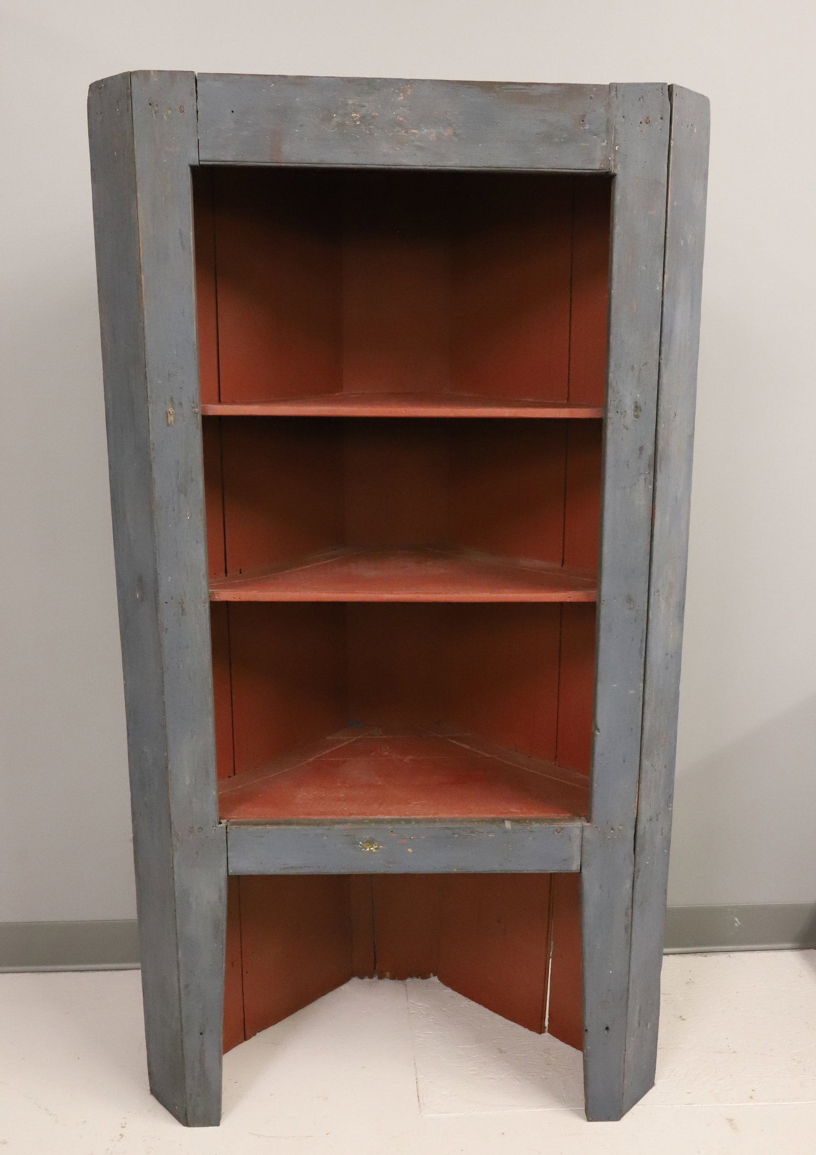 PAINTED WOODEN CORNER CUPBOARD: OPEN CUPBOARD PAINTED BLUE WITH RED INTERIOR. THREE SHELVES WITH INDENTATIONS FOR PLATES. 60" X 32" X 15". PLEASE READ CAREFULLY - ITEMS MUST BE PAID FOR THROUGH LIVE AUCTIONEERS OR WITH CASH OR CHECK