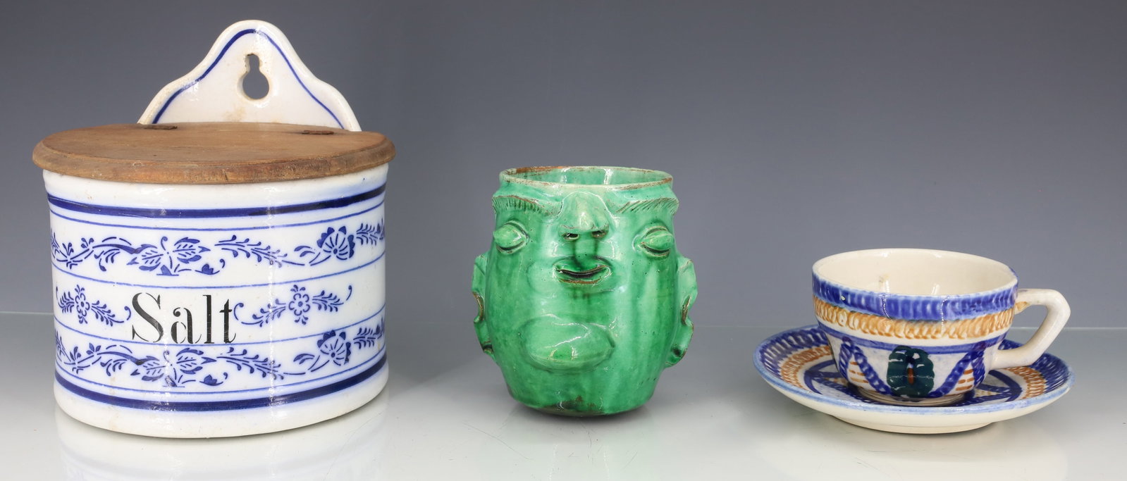 GERMAN SALT CROCK AND POTTERY: BLUE ONION "SALT" HANGING WALL BOX W/ WOODEN LID. PLUS, GREEN GLAZED FACE MUG AND DECORATED GERMAN CUP/SAUCER. PLEASE READ CAREFULLY - ITEMS MUST BE PAID FOR THROUGH LIVE AUCTIONEERS OR WITH CASH OR