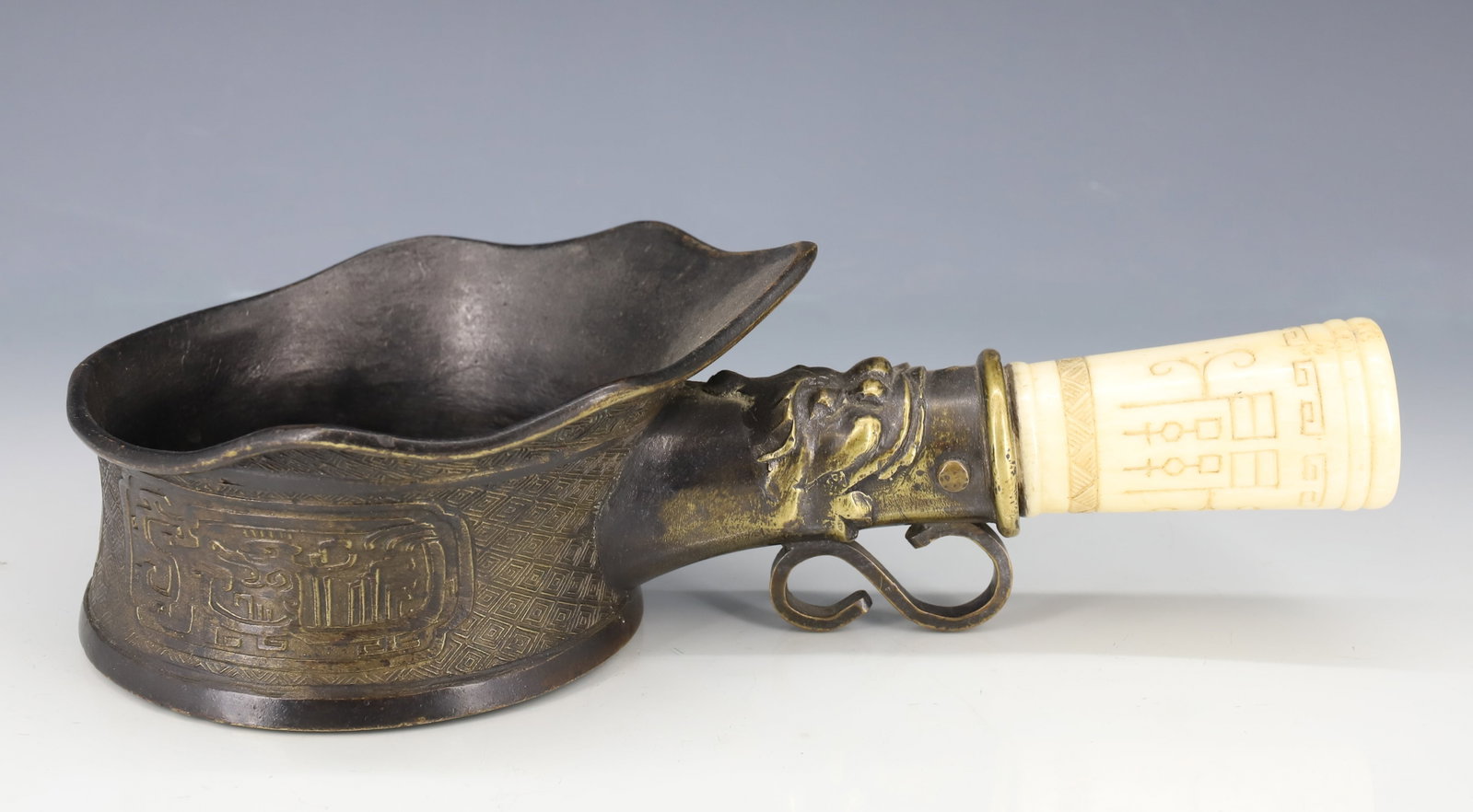 INTRICATE ASIAN PAN IRON: CARVED BONE HANDLE WITH GEOMETRIC DESIGN. FIGURAL BRASS SHAFT WITH APPLIED "S" HOOK. SCALLOPED PAN WITH ASIAN CHARACTER MARKS AND GEOMETRIC DESIGN. 10" L. PLEASE READ CAREFULLY - ITEMS MUST BE PAID FO