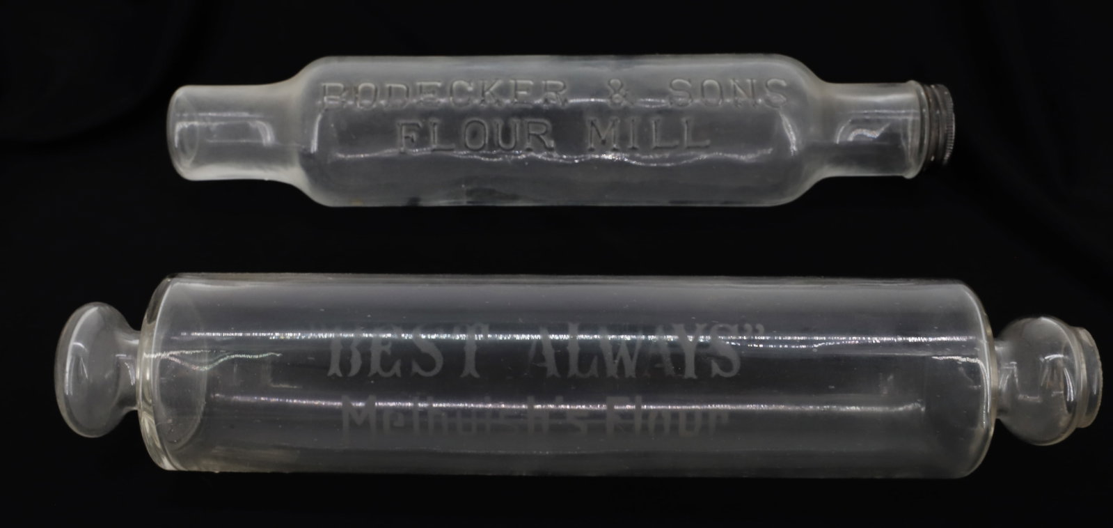 (2) GLASS ADVERTISING ROLLING RINS: ONE EMBOSSED; "BODECKER & SONS FLOUR MILL" 13 3/4" WITH BLACK CAP ON END AND ETCHED "BEST ALWAYS, MELHUISH'S FLOUR" 14 1/4" PLEASE READ CAREFULLY - ITEMS MUST BE PAID FOR THROUGH LIVE AUCTIONEERS OR W