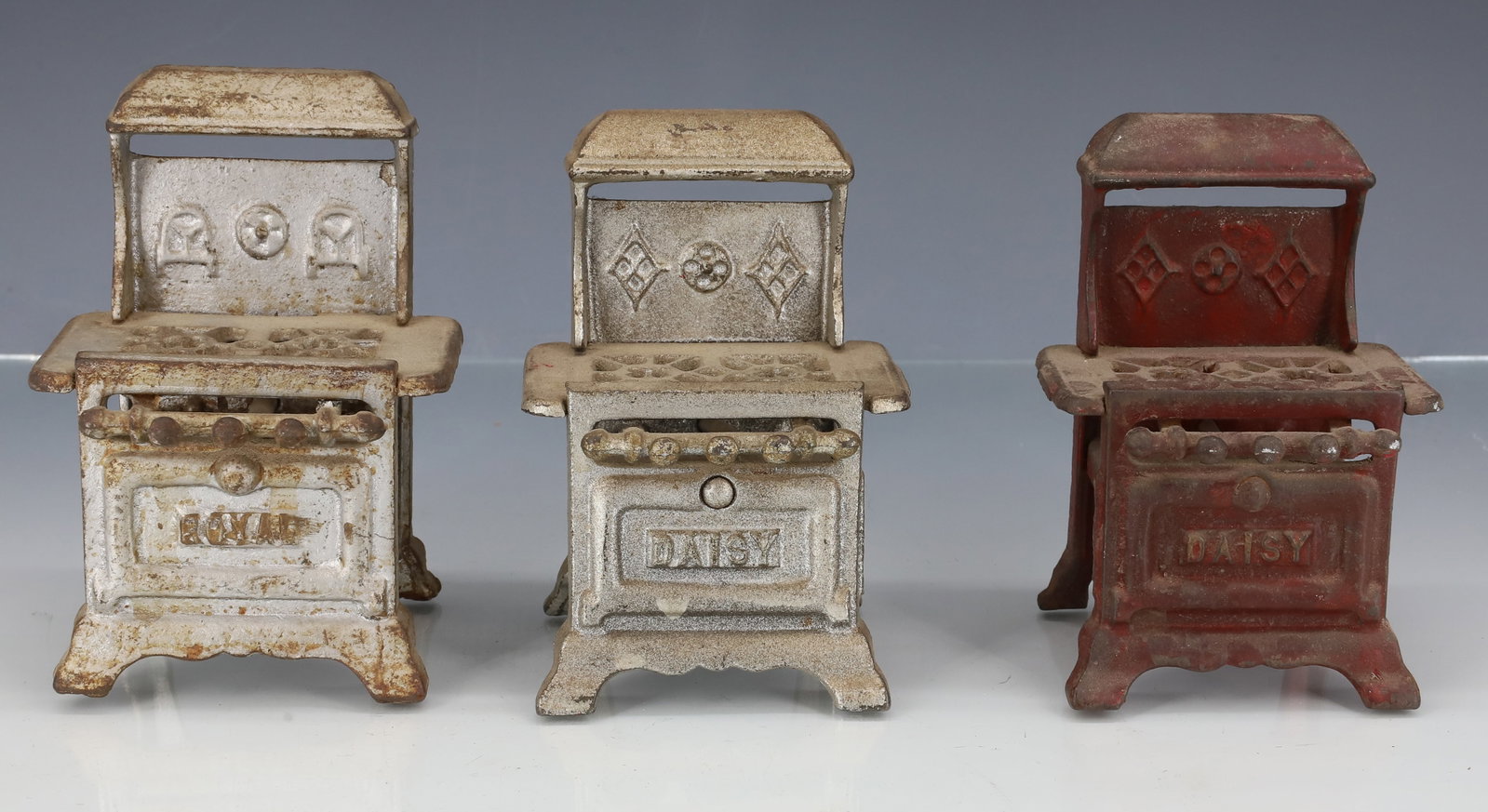 (3) CAST IRON MINIATURE STOVES: PAINTED SILVER AND RED, EXAMPLES ARE MARKED; ROYAL AND DAISY - LARGEST 4 3/8" X 3 1/8" X 2 1/2" PLEASE READ CAREFULLY - ITEMS MUST BE PAID FOR THROUGH LIVE AUCTIONEERS OR WITH CASH OR CHECK IN PERSON 