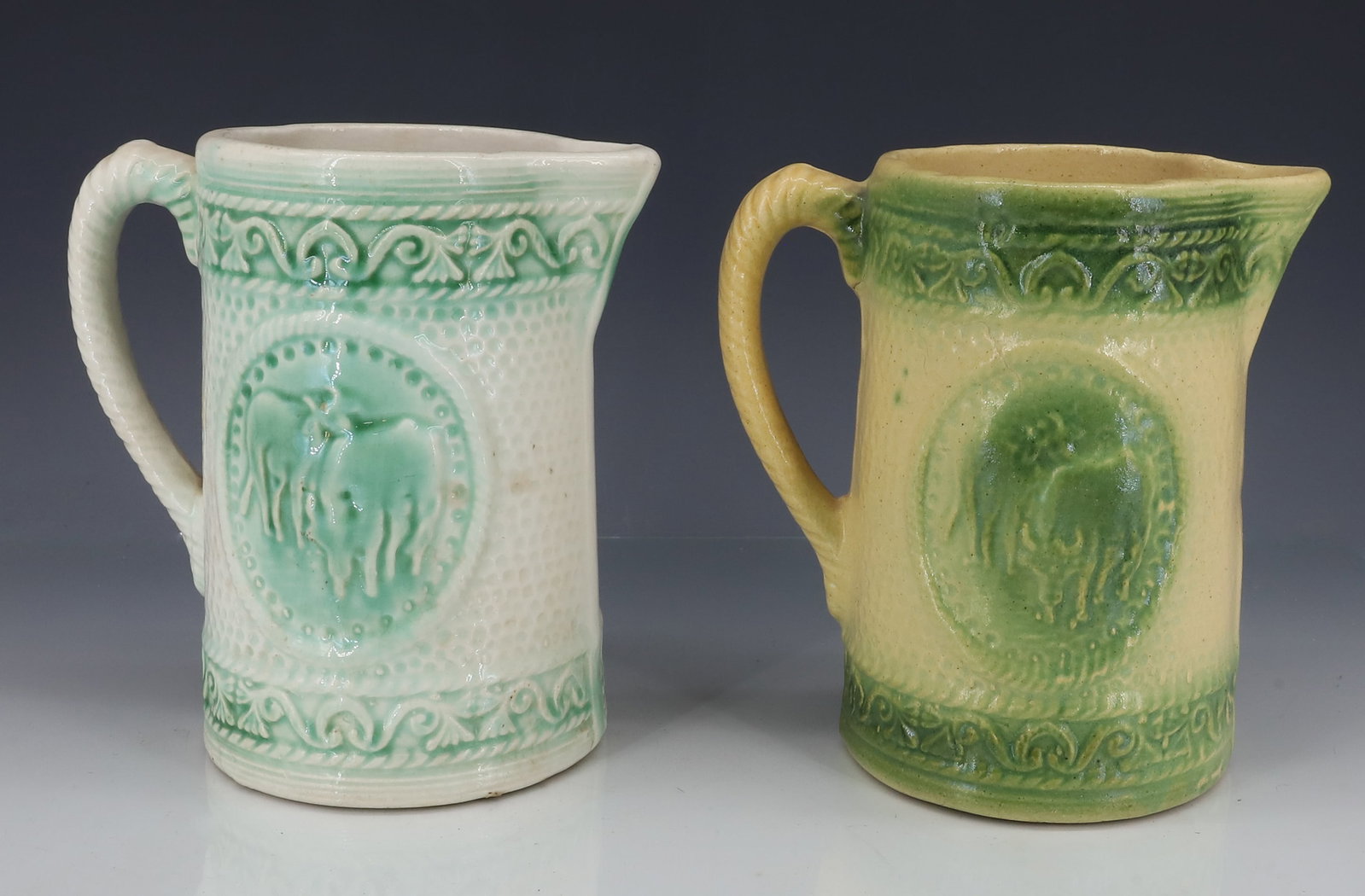 (2) STONEWARE PITCHERS: MOLDED GREEN AND WHITE PITCHERS WITH COW MOTIFS, 6 3/4" H - GREEN AND PALE YELLOW IN COLOR PLEASE READ CAREFULLY - ITEMS MUST BE PAID FOR THROUGH LIVE AUCTIONEERS OR WITH CASH OR CHECK IN PERSON -