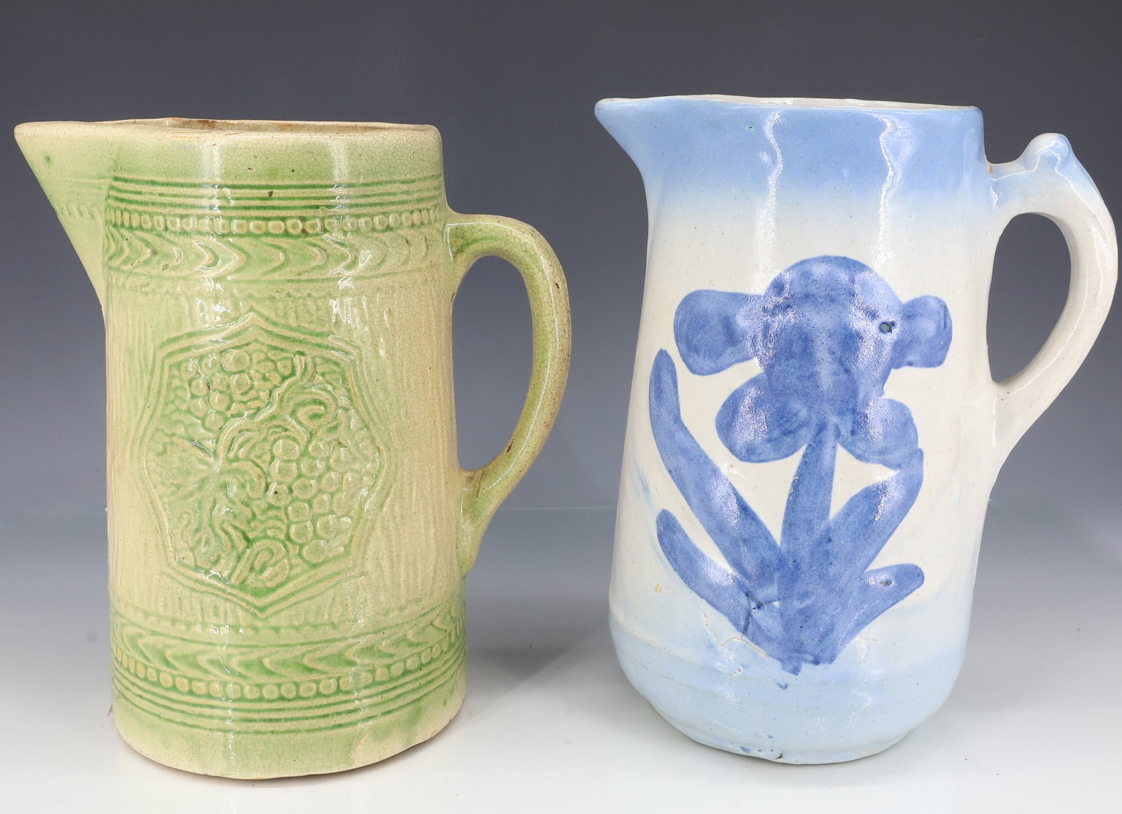 (2) STONEWARE PITCHERS: BLUE AND WHITE SALT GLAZE PITCHER WITH FLORAL DECORATION 8 1/2" - YELLOW AND GREEN MOLDED PITCHER WITH GRAPE BUNCH MOTIF 8" H PLEASE READ CAREFULLY - ITEMS MUST BE PAID FOR THROUGH LIVE AUCTIONEERS OR