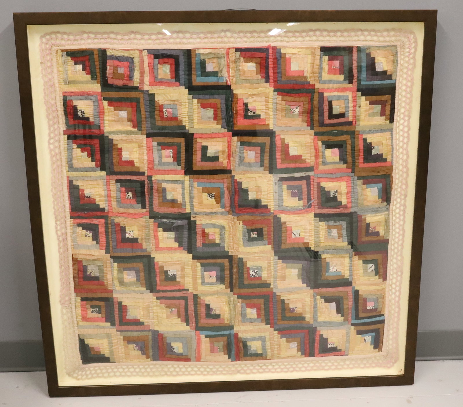FRAMED ANTIQUE CRIB QUILT: LOG CABIN PATTERN DONE IN VARIOUS SILK FABRICS. CONTEMPORARY FRAME TO HANG FOR DISPLAY. 42" X 41 3/4". PLEASE READ CAREFULLY - ITEMS MUST BE PAID FOR THROUGH LIVE AUCTIONEERS OR WITH CASH OR CHECK IN