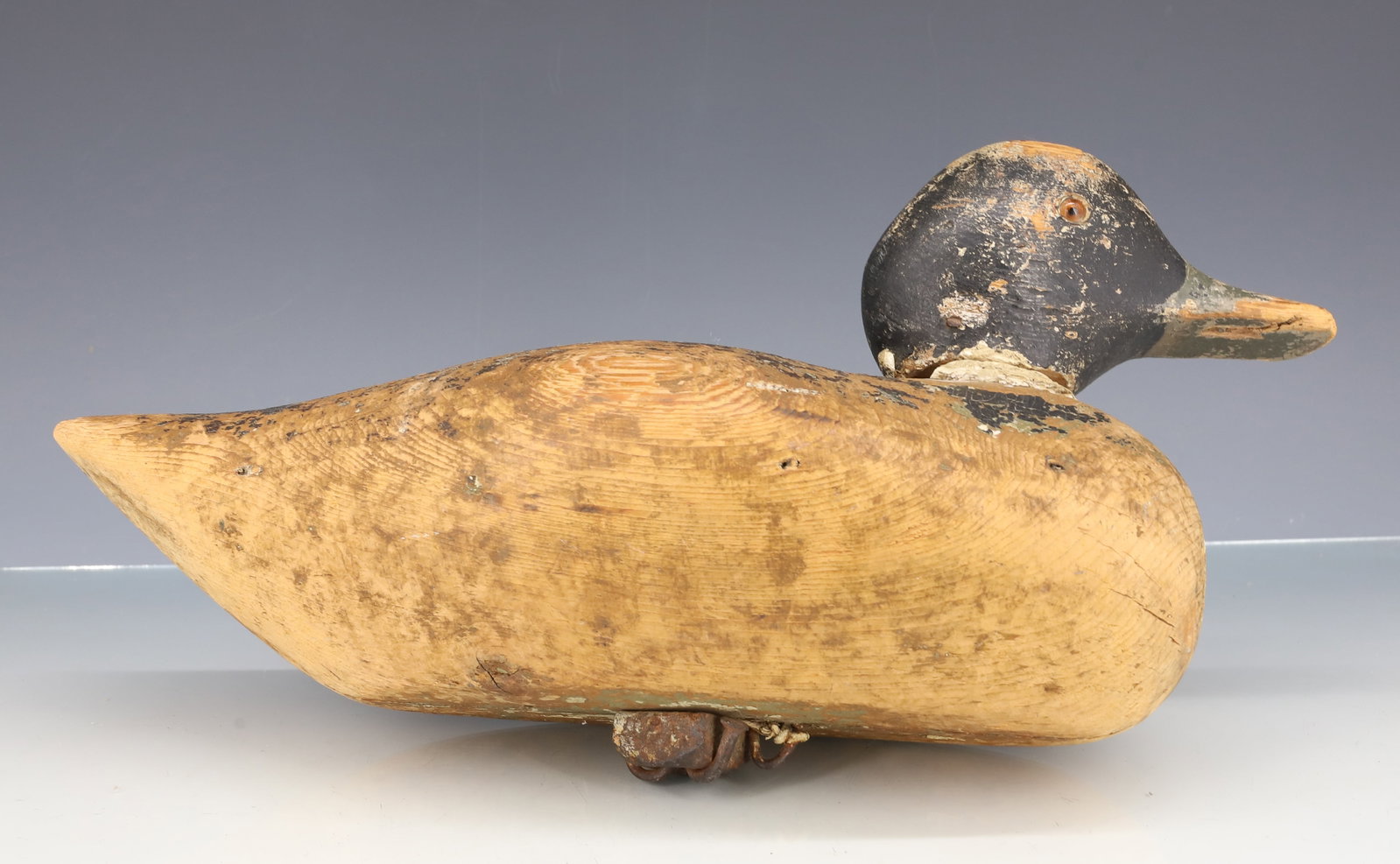 FOLK ART WOODEN DUCK DECOY: SOLID BODY WITH IRON "NUT" WEIGHT ON BOTTOM. GLASS EYES. REMNANTS OF PAINTED SURFACE. 13 3/8" L. PLEASE READ CAREFULLY - ITEMS MUST BE PAID FOR THROUGH LIVE AUCTIONEERS OR WITH CASH OR CHECK IN PERSON