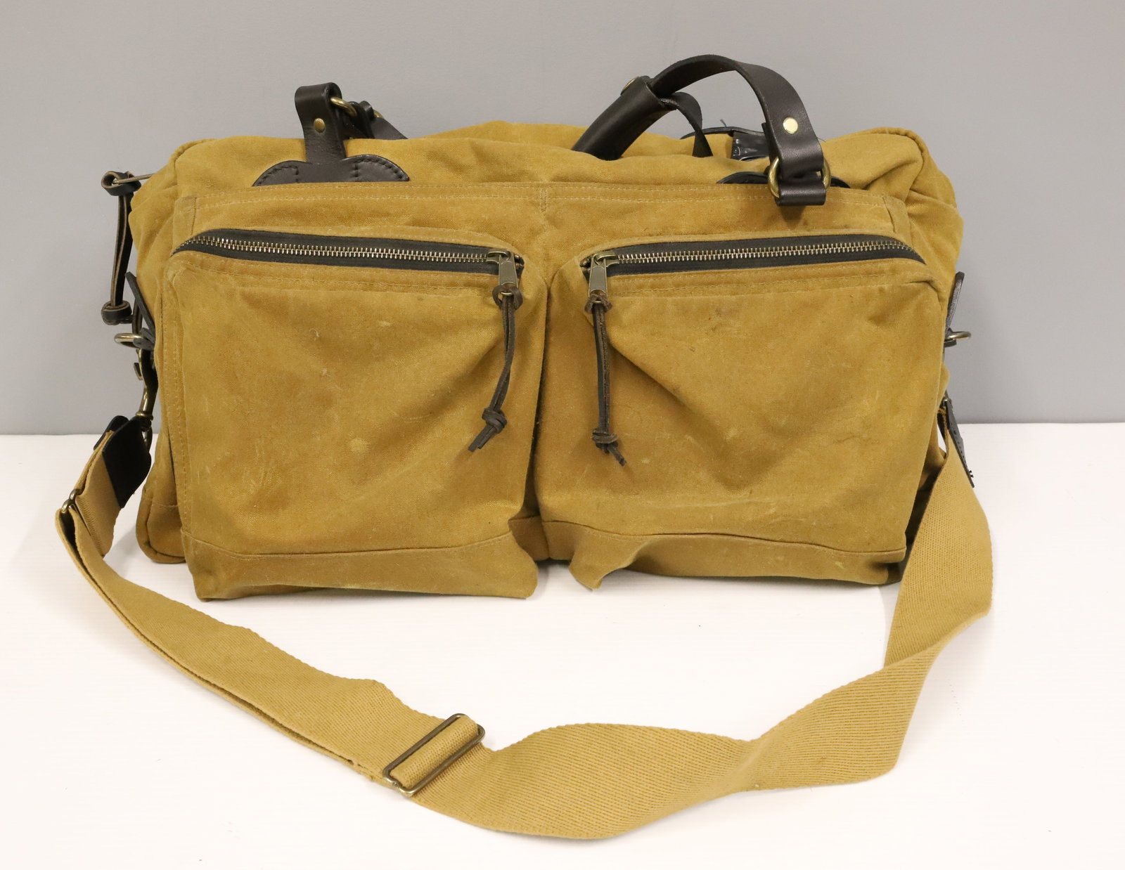 FILSON 48-HOUR TIN CLOTH DUFFLE BAG: COTTON INTERIOR WITH WOVEN COTTON SHOULDER STRAP. LEATHER HANDLES. 11" X 18". PLEASE READ CAREFULLY - ITEMS MUST BE PAID FOR THROUGH LIVE AUCTIONEERS OR WITH CASH OR CHECK IN PERSON - Terms for