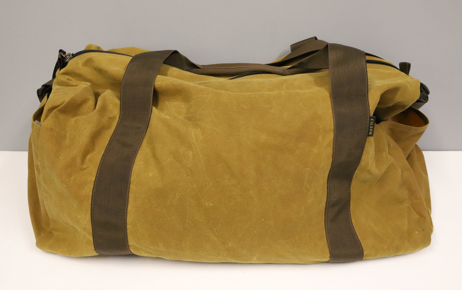 FILSON FIELD DUFFLE: DARK TAN BROWN. LINED INTERIOR. NYLON SHOULDER STRAP. 22" L. PLEASE READ CAREFULLY - ITEMS MUST BE PAID FOR THROUGH LIVE AUCTIONEERS OR WITH CASH OR CHECK IN PERSON - Terms for Purchasing and