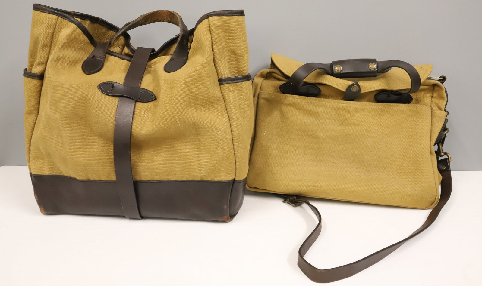 (2) FILSON TWILL BAGS: LARGE TOTE 17" X 16" WITH BRIEFCASE 12" X 16". LEATHER STRAPS AND HANDLES. BRIEFCASE HAS SHOULDER STRAP. PLEASE READ CAREFULLY - ITEMS MUST BE PAID FOR THROUGH LIVE AUCTIONEERS OR WITH CASH OR CHECK