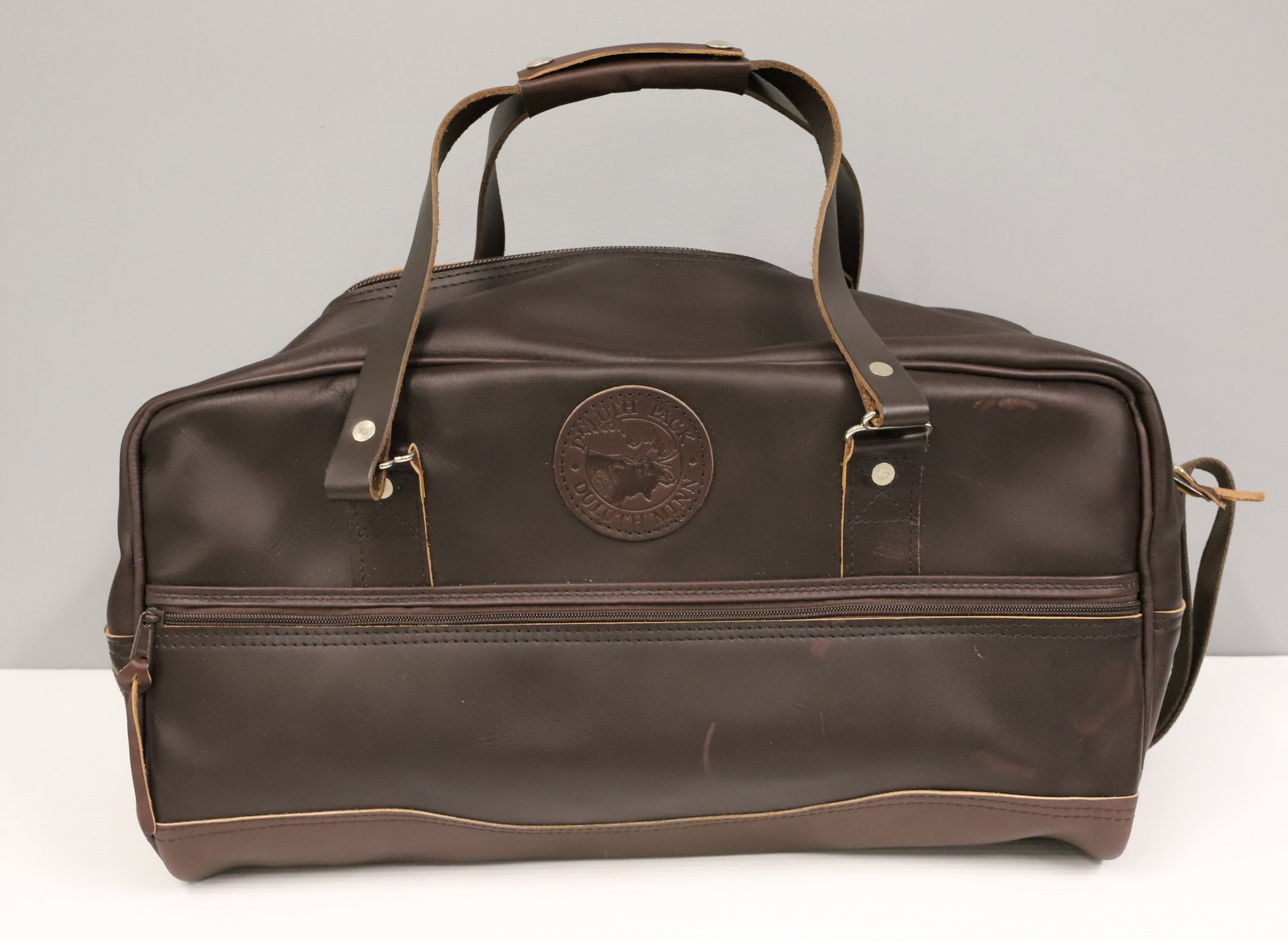 (2) DULUTH LEATHER DUFFEL BAGS: LEATHER DUFFEL BAGS WITH WOVEN COTTON SHOULDER STRAPS. ONE HAS FLAP OVER TOP ZIPPER. 20" X 11" PLEASE READ CAREFULLY - ITEMS MUST BE PAID FOR THROUGH LIVE AUCTIONEERS OR WITH CASH OR CHECK IN PERSON -