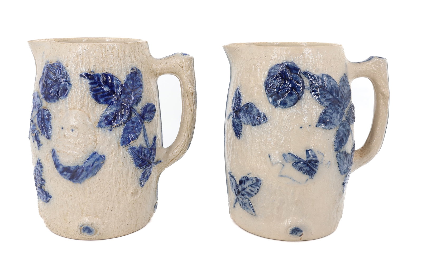 (2) WHITE'S UTICA STONEWARE PITCHERS: MOLDED FAUX-BARK. BOTH HAVE PROFILE OF A MAN ON EITHER SIDE. BLUE HIGHLIGHTED LEAF AND FLORAL DESIGN. 8 1/4" H. PLEASE READ CAREFULLY - ITEMS MUST BE PAID FOR THROUGH LIVE AUCTIONEERS OR WITH CASH OR