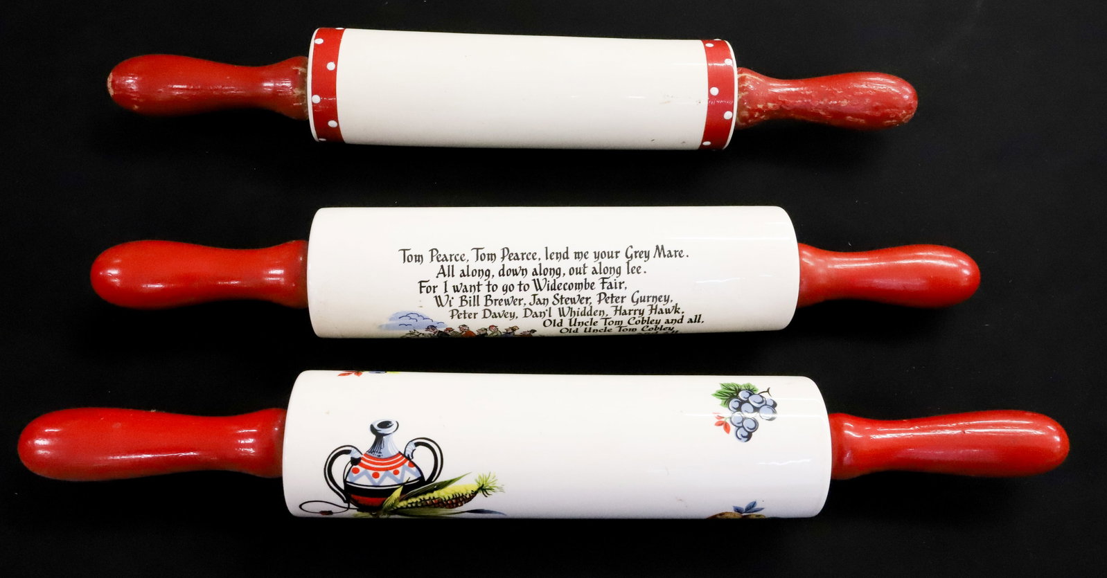 (3) CERAMIC ROLLING PINS: RED PAINTED WOODEN HANDLES. VARIOUS MOTIFS INCLUDING: ENGLISH VERSE WITH CORNISH PASTY, SOUTHWESTERN AND SMALL POLKA DOT DECORATION. LARGEST 18" TOTAL LENGTH. PLEASE READ CAREFULLY - ITEMS MUST BE