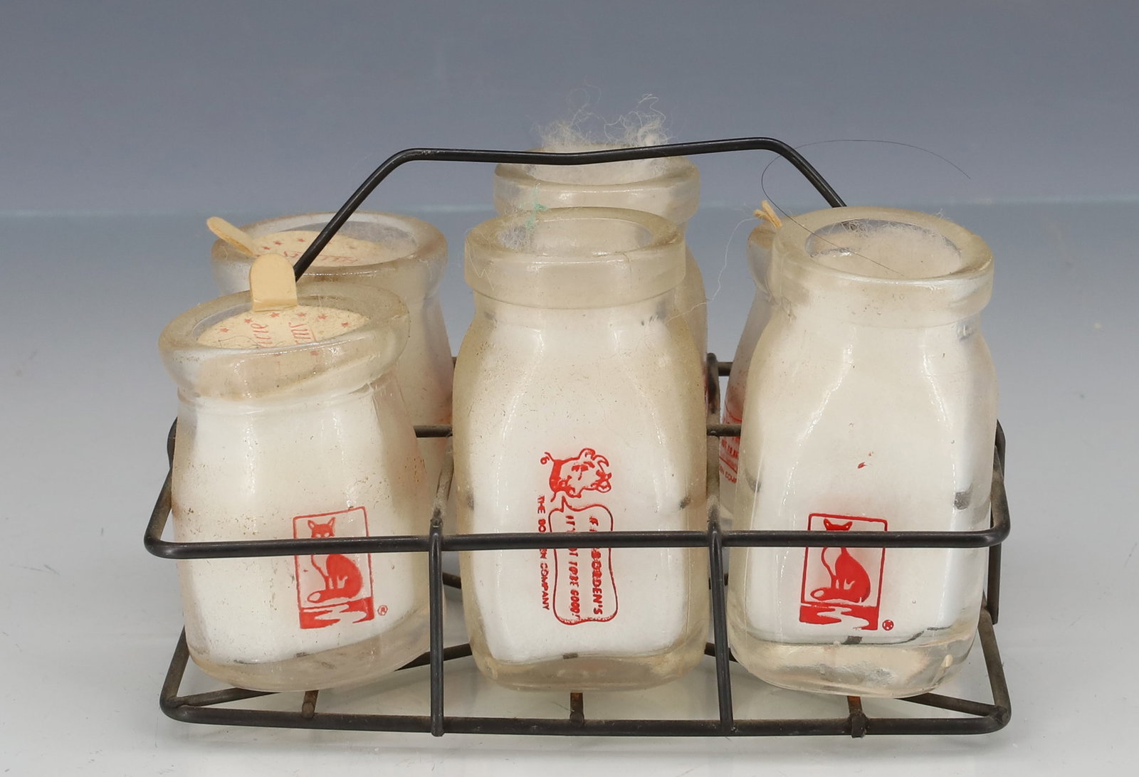 (6) VINTAGE ADVERTISING MILK CREAMERS: GLASS WITH RED ADVERTISING INCLUDING: FOXES DAIRY CARTHAGE, BORDENS, MULLERS. WITH WIRE CARRIER 4 1/4" L. PLEASE READ CAREFULLY - ITEMS MUST BE PAID FOR THROUGH LIVE AUCTIONEERS OR WITH CASH OR CHECK