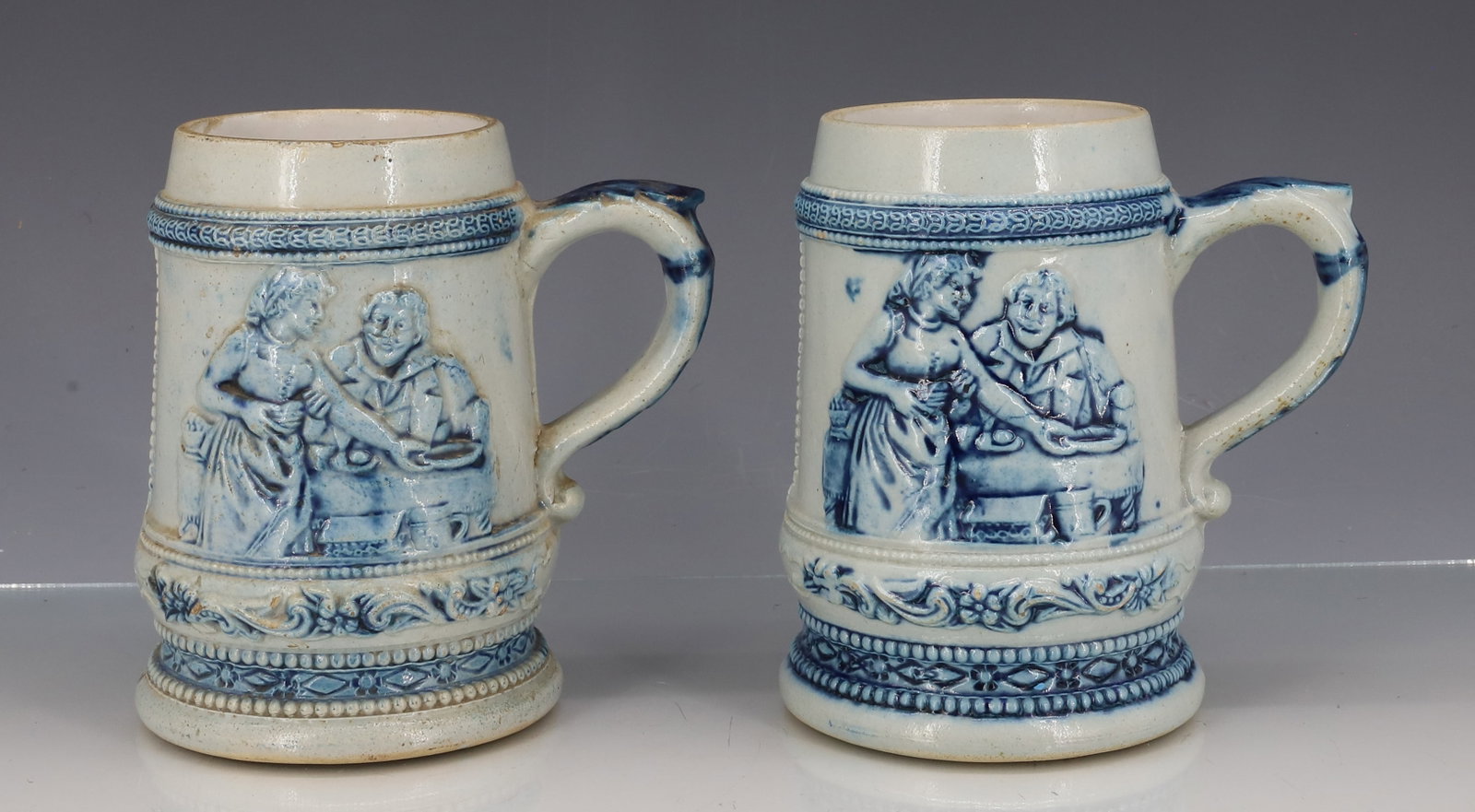 (2) WHITE'S UTICA STONEWARE MUGS: MAN AND WIFE AT TABLE WITH VERSE ON OPPOSITE SIDE. (OTHER HAS GRIFFIN). BOTH MRKD. 35 ON BOTTOM. 5" H. PLEASE READ CAREFULLY - ITEMS MUST BE PAID FOR THROUGH LIVE AUCTIONEERS OR WITH CASH OR CHECK IN 