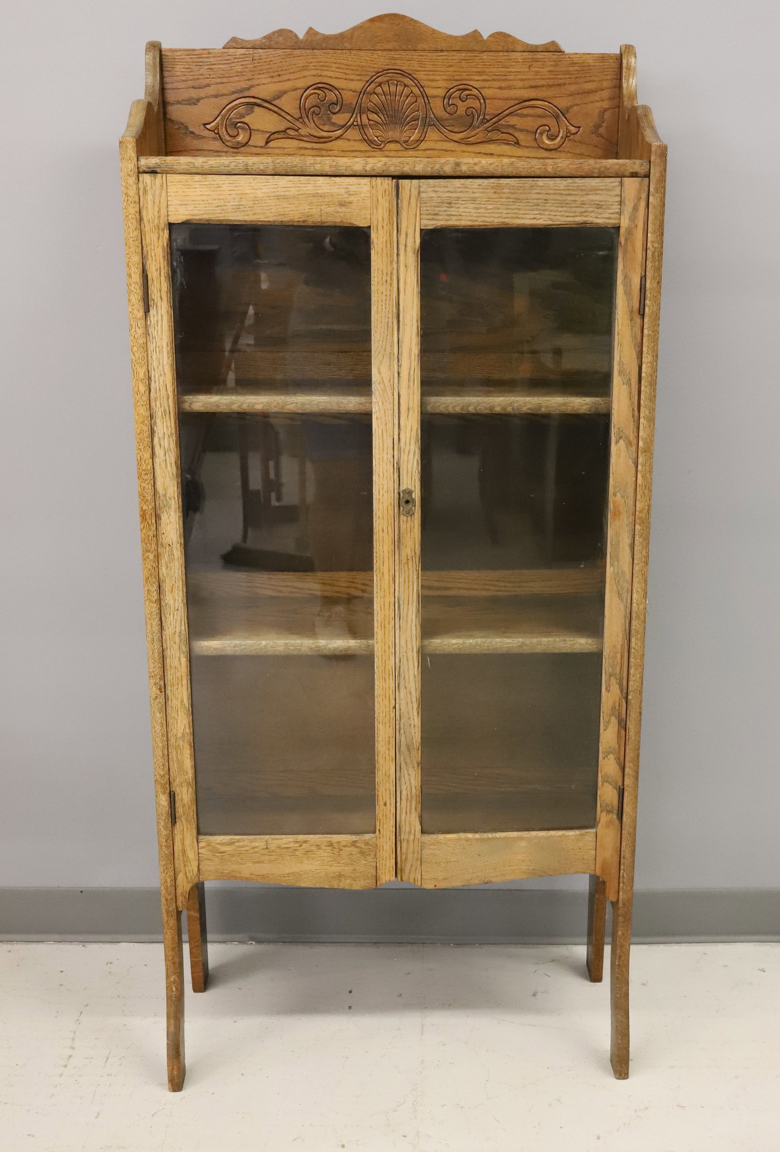 ANTIQUE GLASS DOOR CABINET: TWO GLASS DOORS WITH INTERIOR SHELVES. CARVED DECORATION AT TOP. 56 1/2" X 25 1/2" X 11". PLEASE READ CAREFULLY - ITEMS MUST BE PAID FOR THROUGH LIVE AUCTIONEERS OR WITH CASH OR CHECK IN PERSON - Term