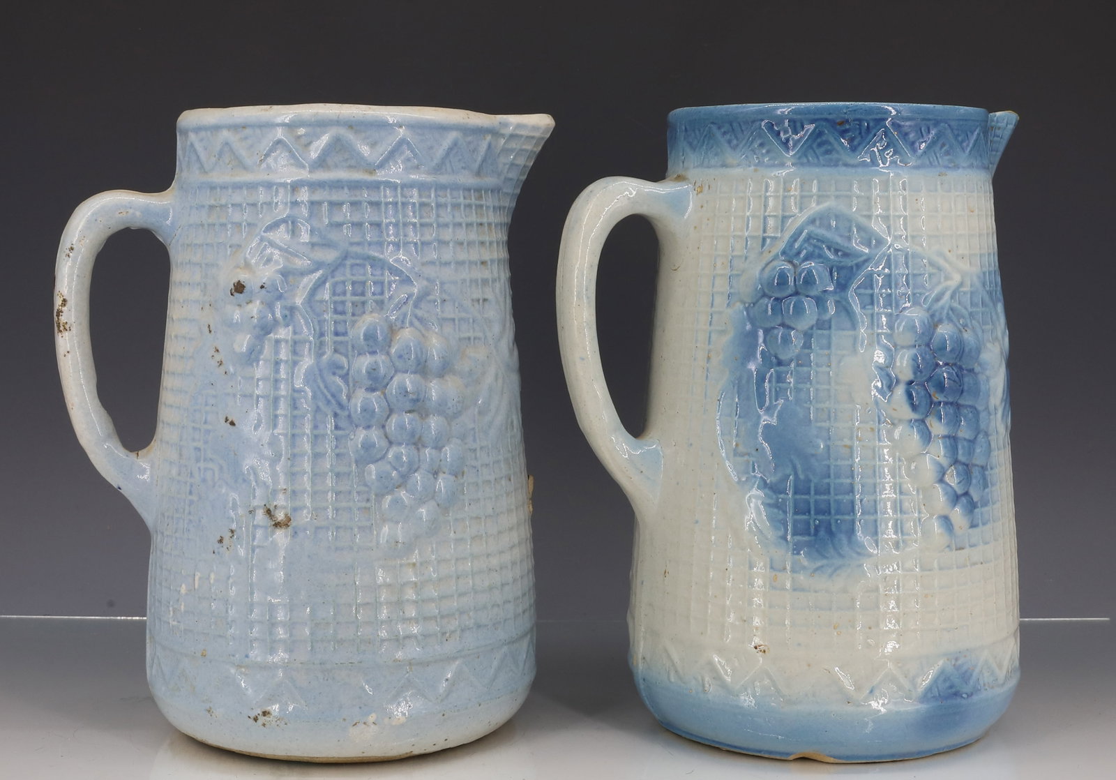 (2) BLUE / WHITE SALT GLAZED PITCHERS: MOLDED FRUIT DECORATION. 9" H. BRIGHTER BLUE COLOR HAS "STAR" MOTIF ON BOTTOM. PLEASE READ CAREFULLY - ITEMS MUST BE PAID FOR THROUGH LIVE AUCTIONEERS OR WITH CASH OR CHECK IN PERSON - Terms for Purch