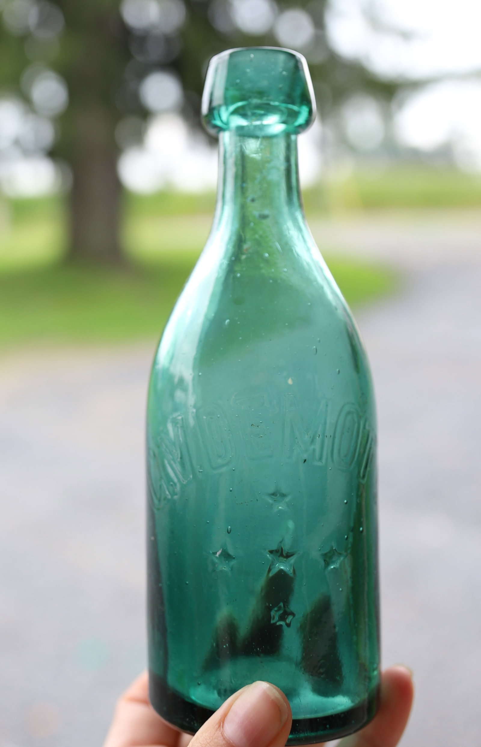 C.V. DEMOTT SODA BOTTLE: GREEN WITH EMBOSSED NAME / FIVE STARS ON FRONT AND INITIALS ON BACK. 7 1/8" H. PLEASE READ CAREFULLY - ITEMS MUST BE PAID FOR THROUGH LIVE AUCTIONEERS OR WITH CASH OR CHECK IN PERSON - Terms for