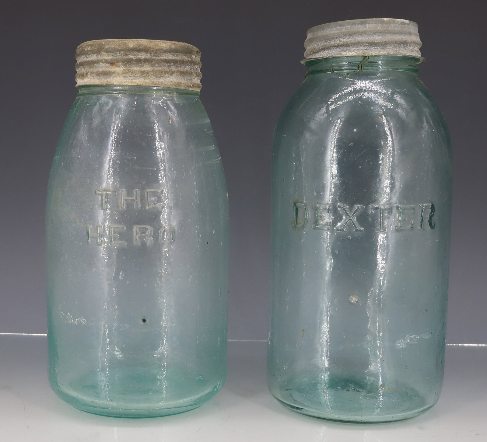 THE HERO AND "DEXTER" FRUIT JARS: TWO LARGE AQUA JARS. "THE HERO" WITH GLASS INSERT LID. 8 7/8" X 4 1/4". WITH, "DEXTER" MRKD. "A" ON BOTTOM. ZINC LID. 9 1/2" X 4 1/4" TOTAL SIZE. PLEASE READ CAREFULLY - ITEMS MUST BE PAID FOR