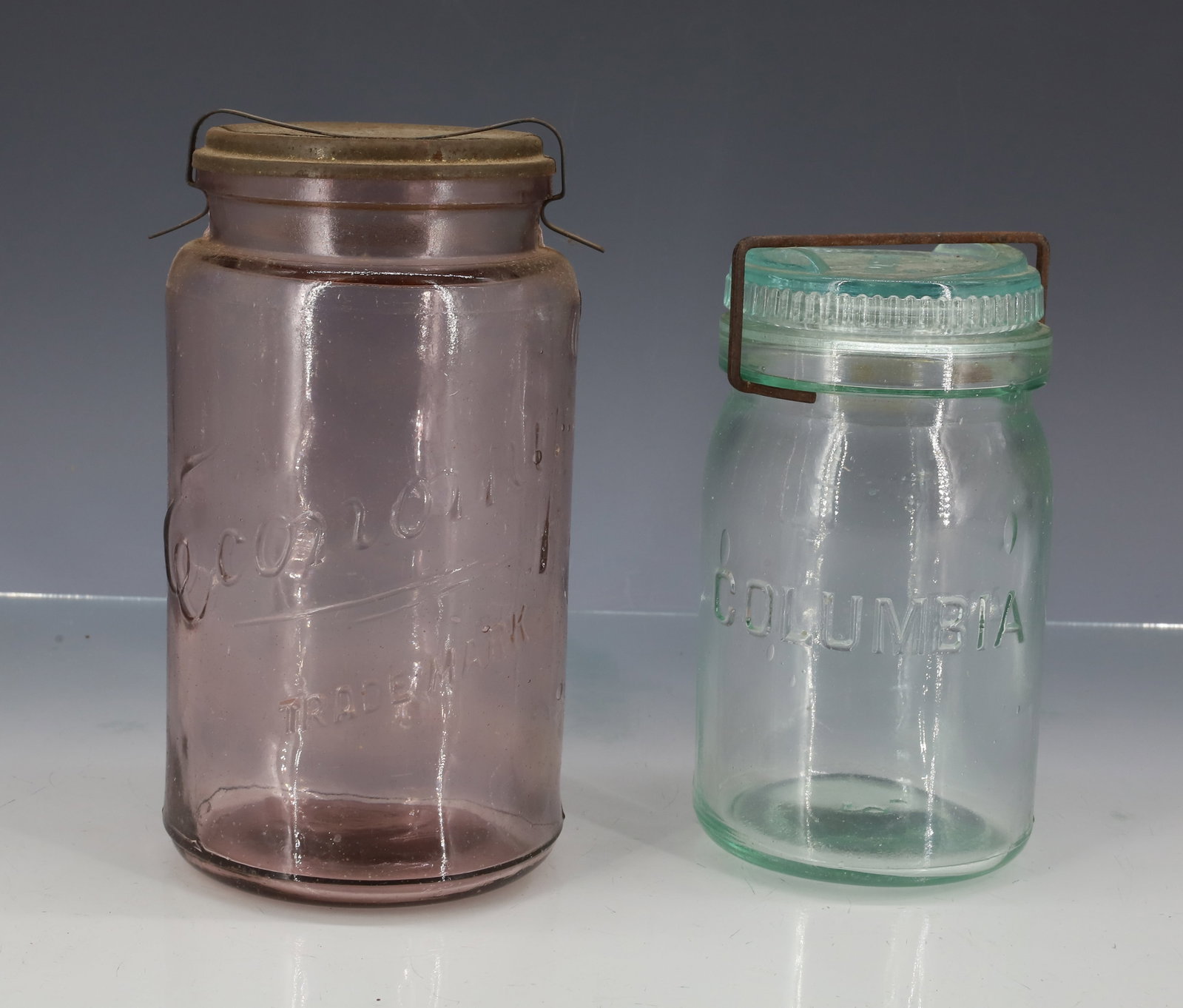 ECONOMY AND "COLUMBIA" FRUIT JARS: CLEAR (AMETHYST) TINT "ECONOMY, TRADE MARK" WITH EMBOSSED METAL LID "ECONOMY JAR, KERR GLASS MFG. CO. " METAL CLOSURE. 6 7/8" H. WITH, "COLUMBIA JAR WITH MATCHING GLASS LID AND WIRE CLOSURE. BOTTOM