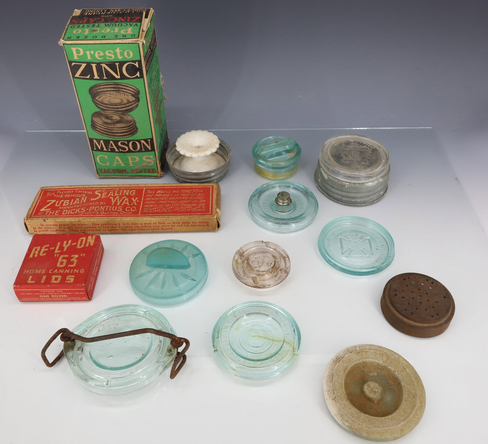 LOT OF FRUIT JAR LIDS, CAPS AND SEALING WAX: VARIETY OF GLASS EMBOSSED FRUIT JAR LIDS. "RE-LY-ON 63 HOME CANNING LIDS" IN BOX. BOX OF "PRESTON ZINC MASON CAPS" (PORCELAIN LINED). BOX OF "ZUBIAN SEALING WAX". PLEASE READ CAREFULLY - ITEMS MUST