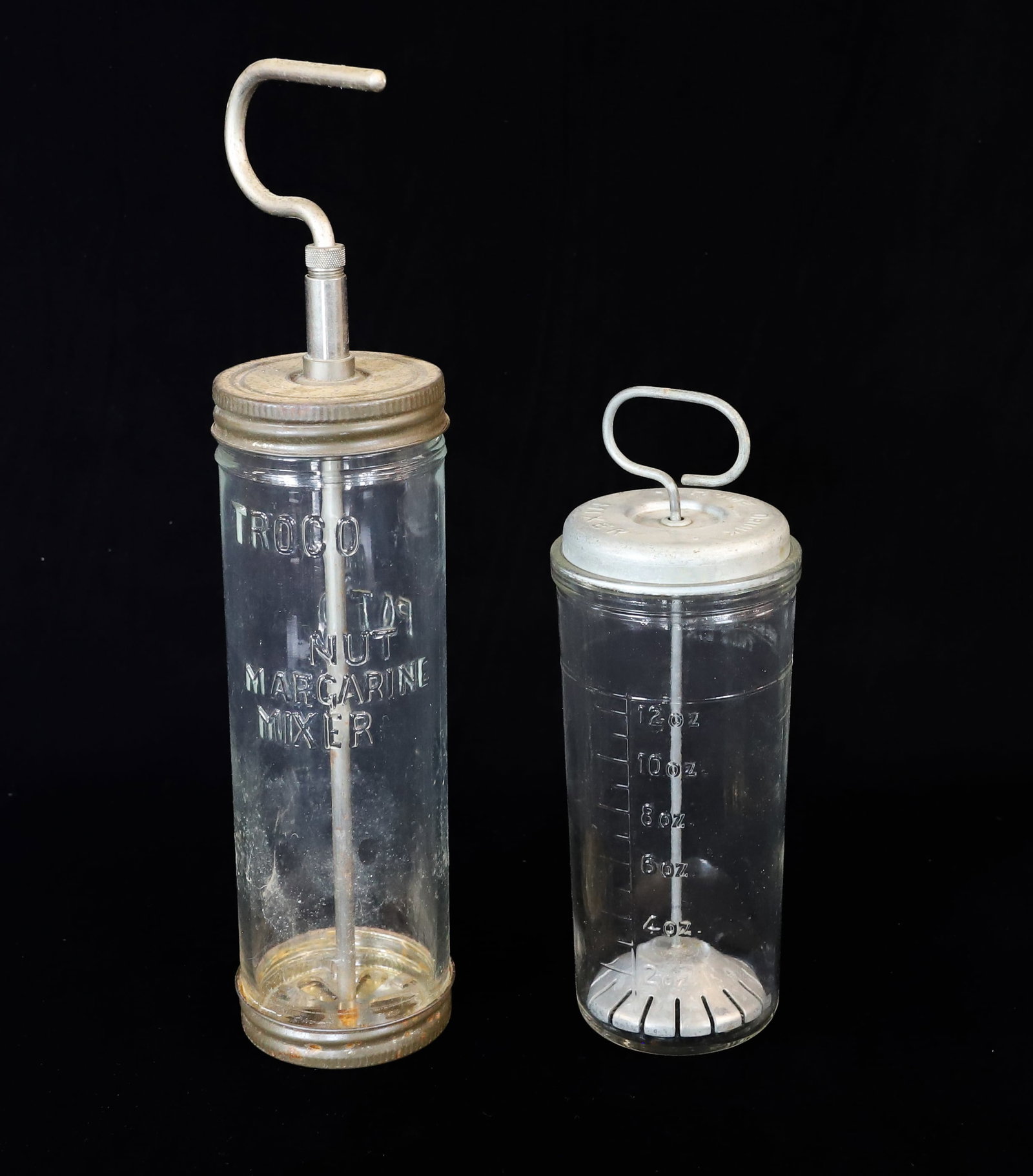 (2) VINTAGE GLASS MIXERS: TROCO NUT MARGARINE MIXER W/ METAL TOP AND BOTTOM. 8 1/2" H. "HOME DRINK MIXER" W/ ALUMINUM TOP. PLEASE READ CAREFULLY - ITEMS MUST BE PAID FOR THROUGH LIVE AUCTIONEERS OR WITH CASH OR CHECK IN